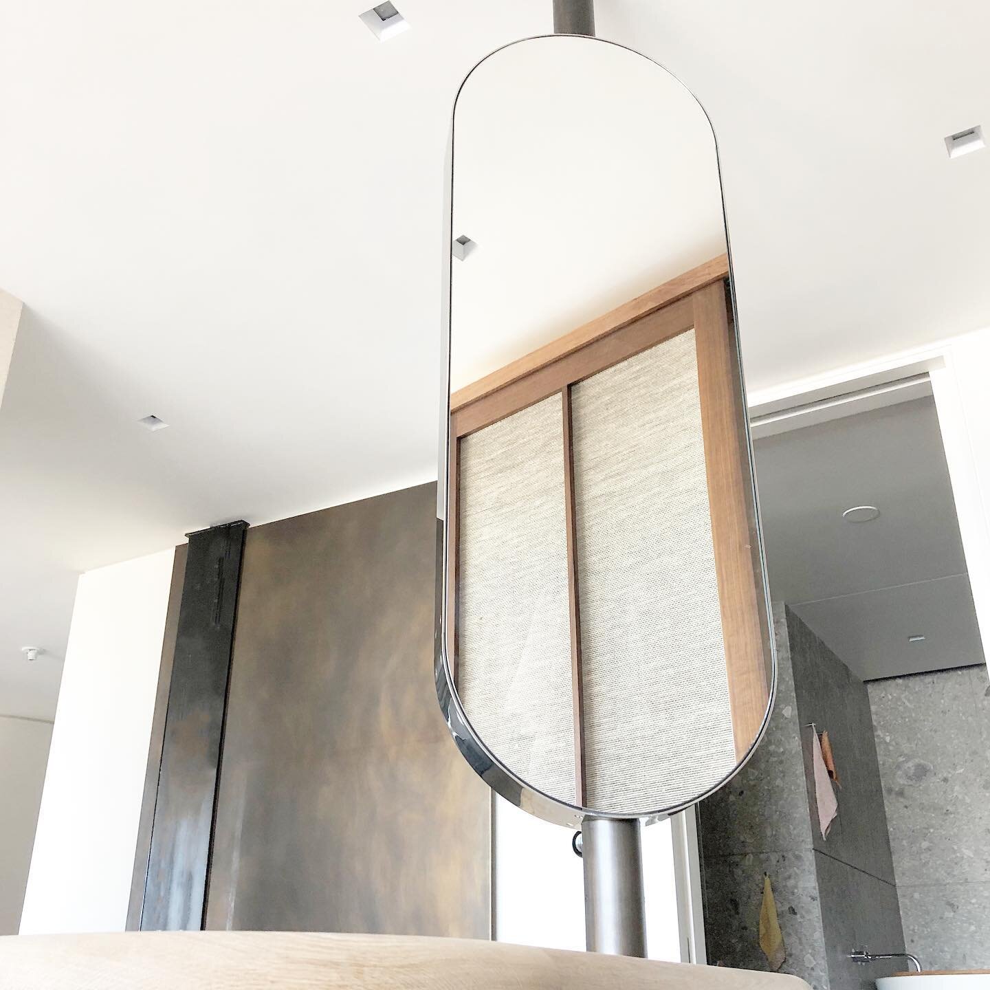 Two sided oval shaped mirror that spins on a custom 3D printed radial bearing and welded bronze axial bearing. It is made in two pieces and surrounds a telecom line. It sits atop a cabinet. The outside is polished stainless and the tube that runs thr