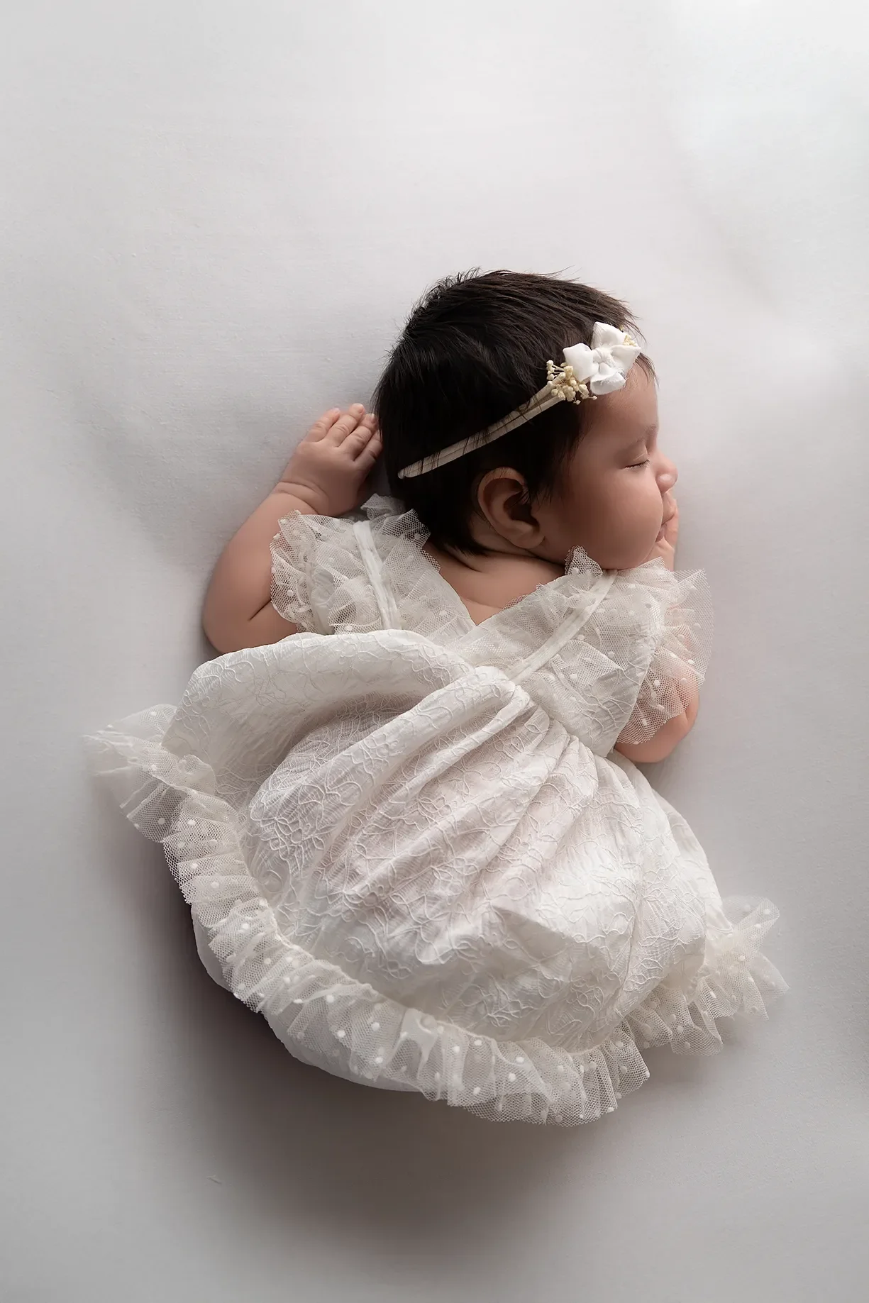  Newborn baby girl photographed in a Glendale California studio with soft neutral tones and dressed in a white lace dress. 