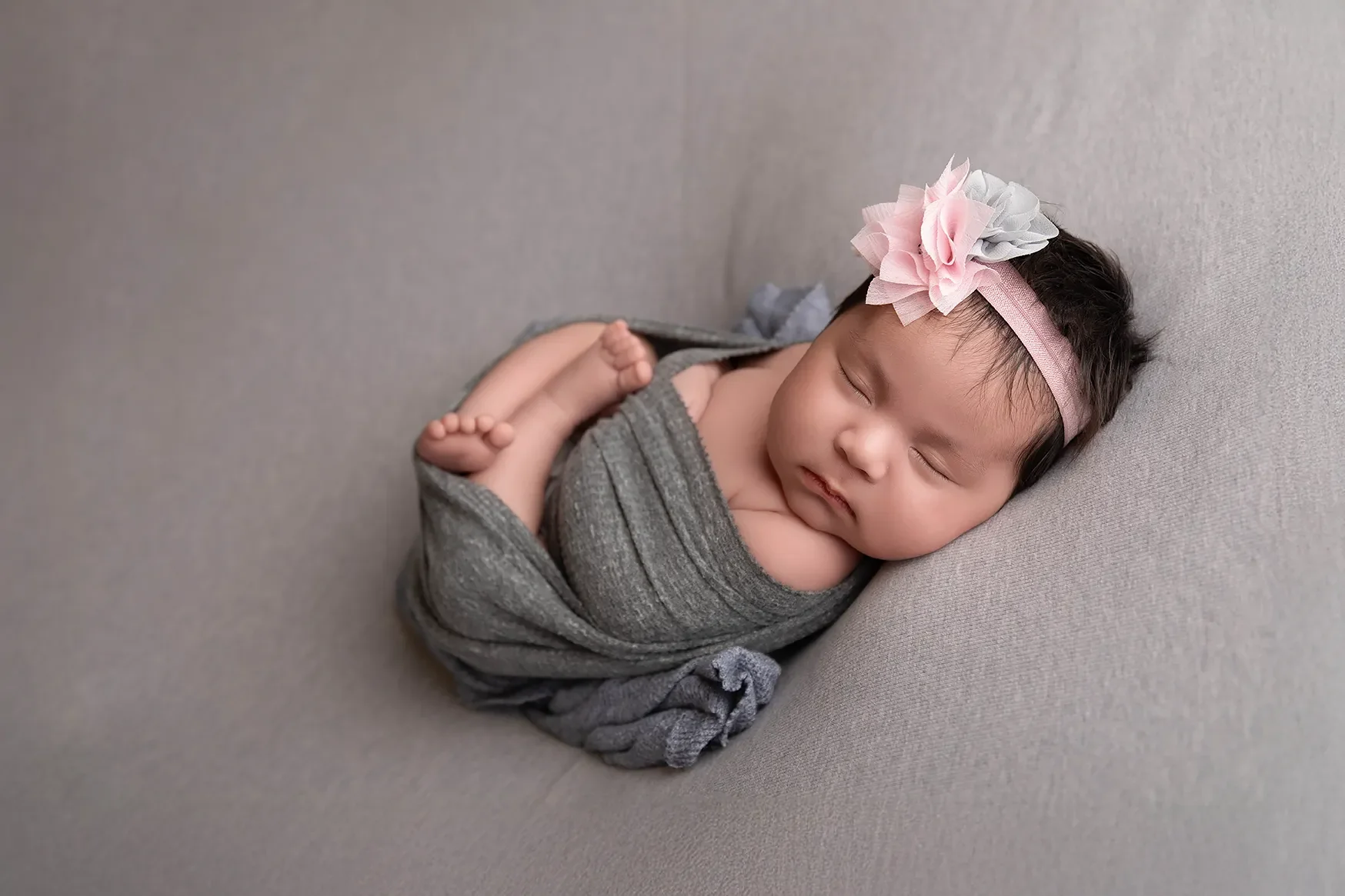  Newborn baby girl photographed in a Glendale California studio with neutral tones on a grey blanket with matching headband. 