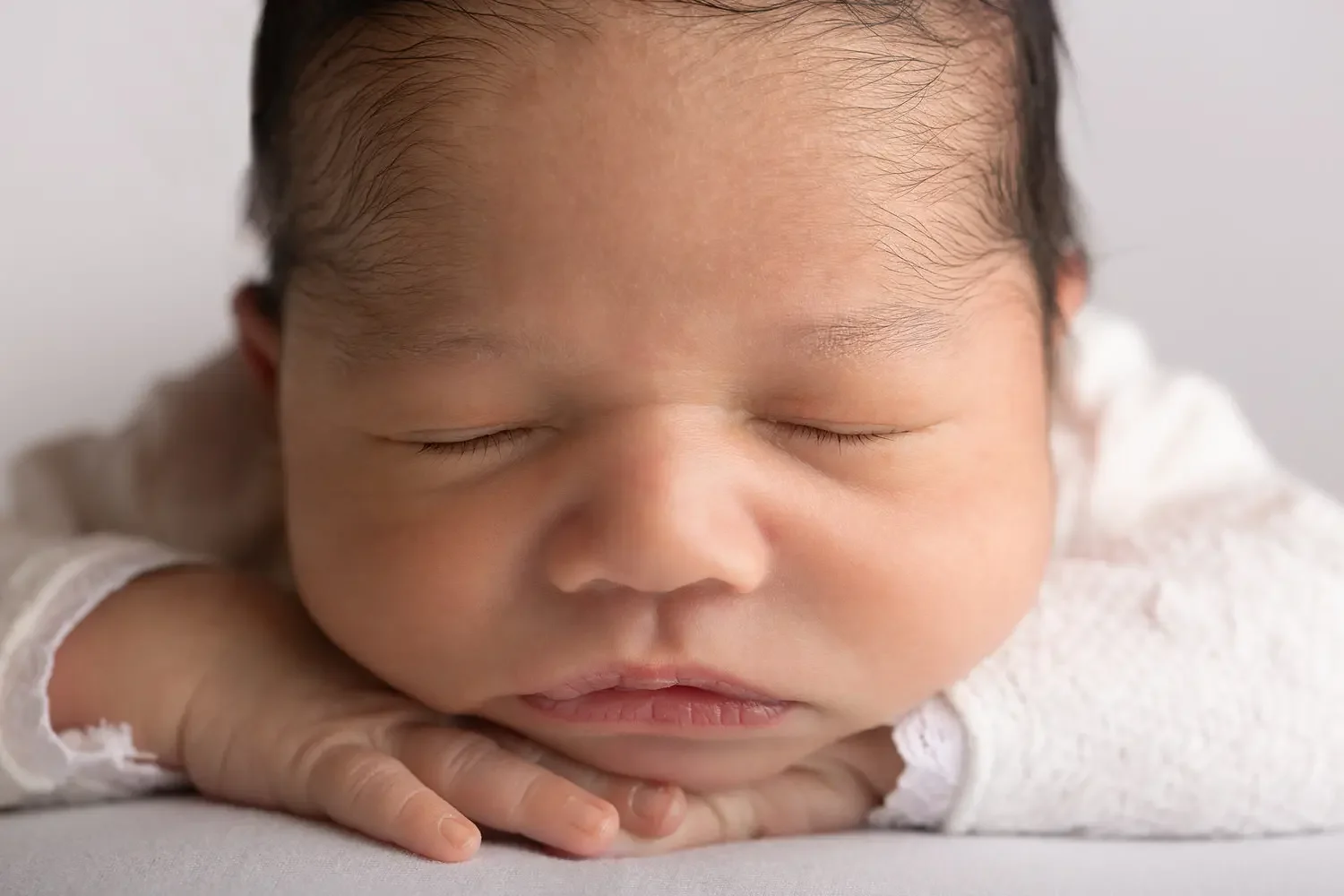  Close up on newborn boy’s face. Chin on hands pose. 