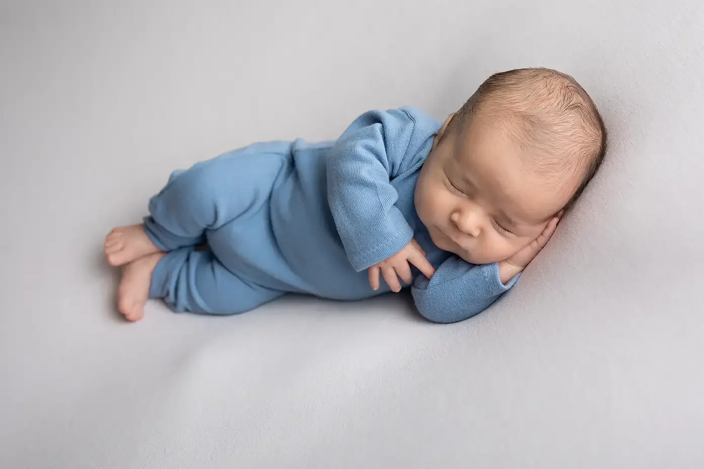 Newborn boy in blue romper sleeping on side in Glendale newborn photography studio