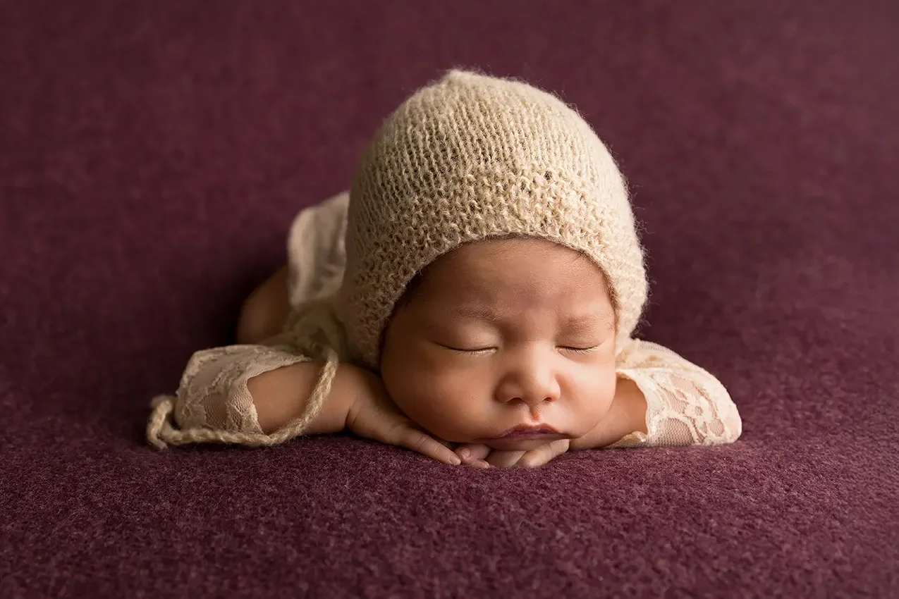 Newborn girl in lace romper chin on hands