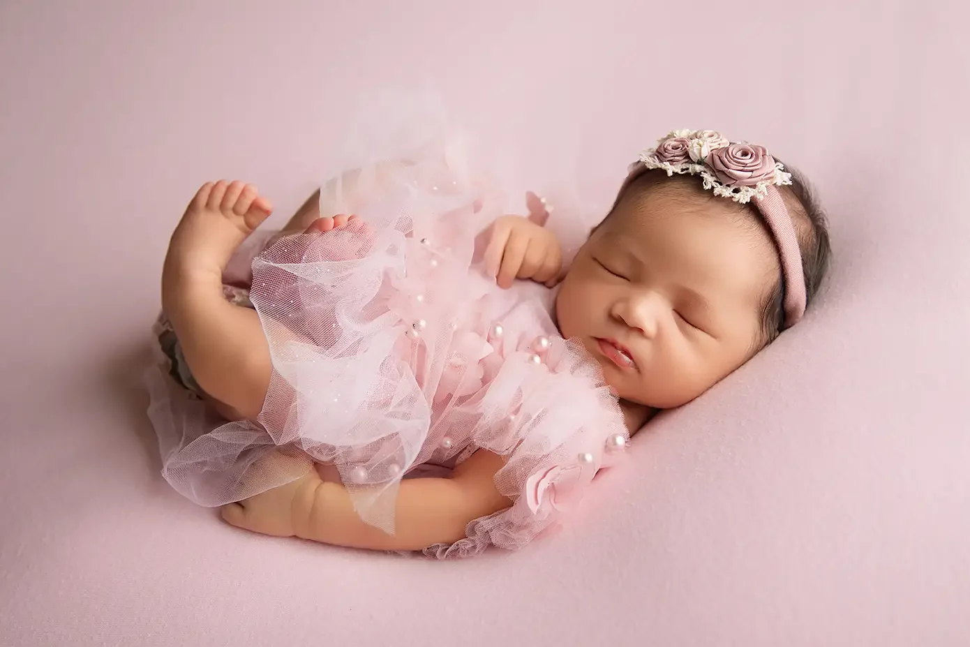 Sleeping newborn baby girl in a pink outfit and floral headband during a Los Angeles newborn photography session.