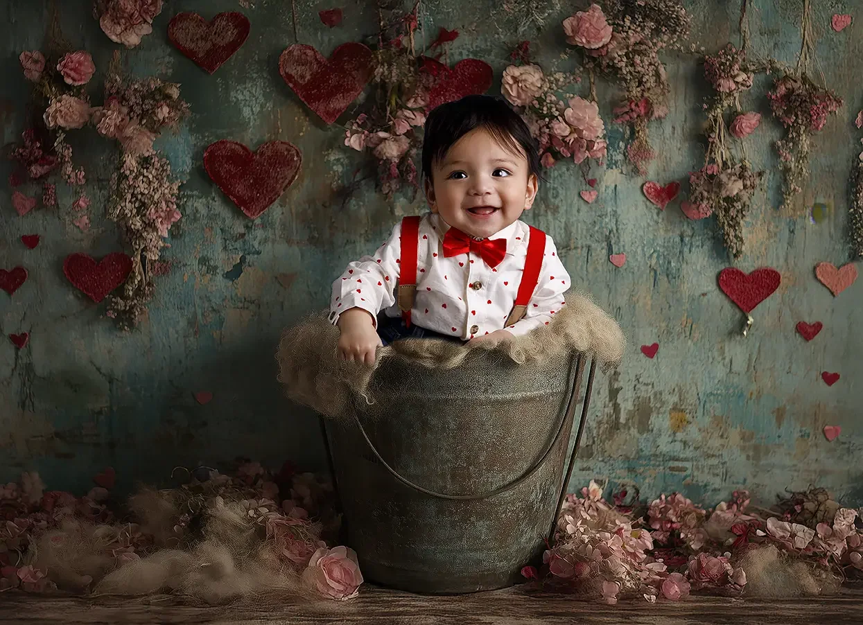 Smiling baby boy sitting in a vintage bucket with red hearts and flowers during a baby milestone photography session in Los Angeles.