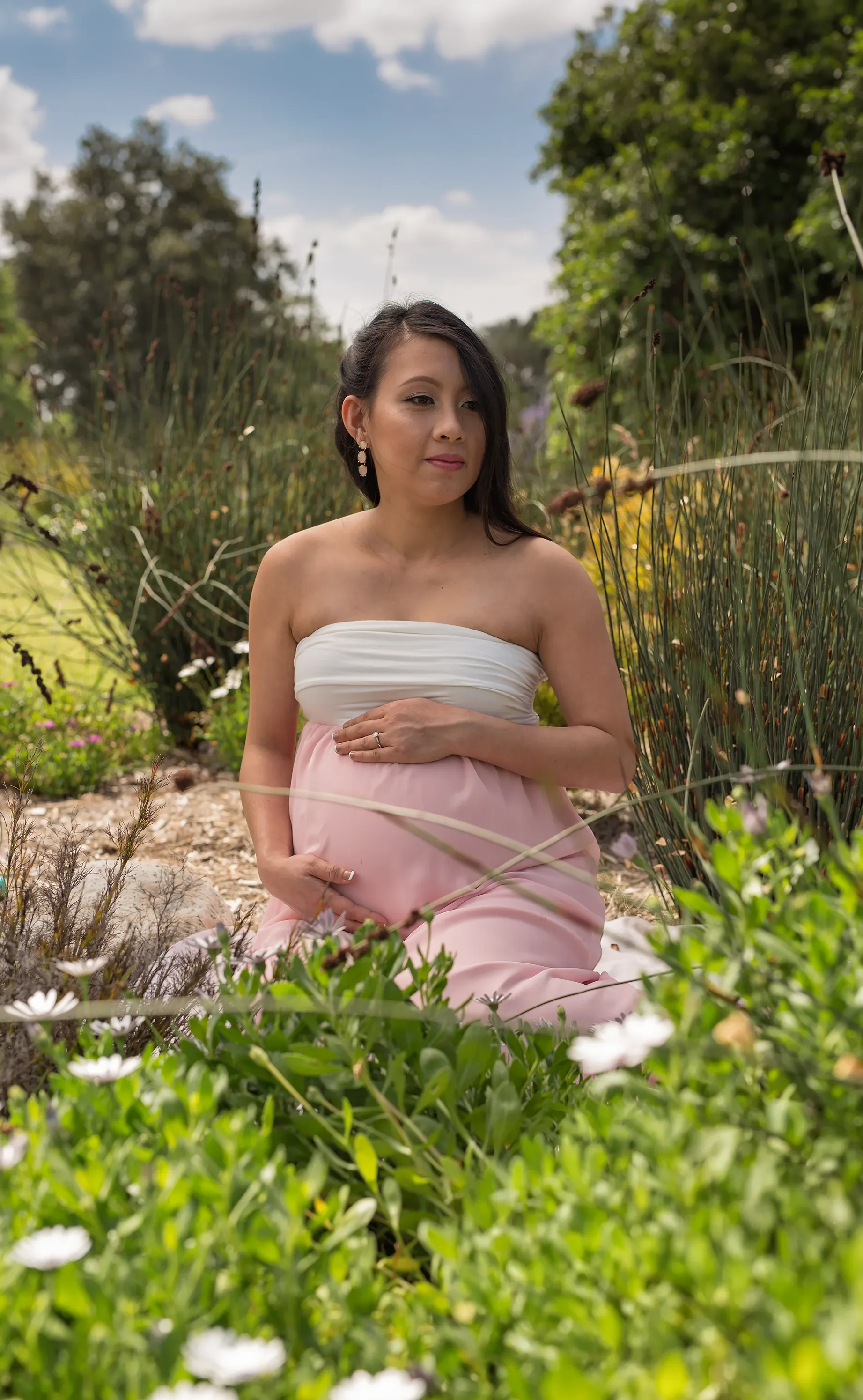 Expecting mother in a pink maternity gown posing among flowers and greenery for an outdoor maternity portrait in Los Angeles.