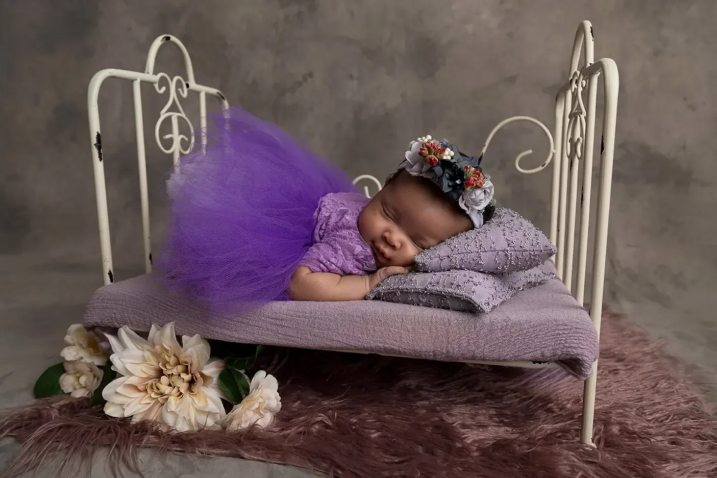 Sleeping newborn baby posed on a vintage bed in a purple outfit during a professional newborn photography session in Los Angeles near Glendale.