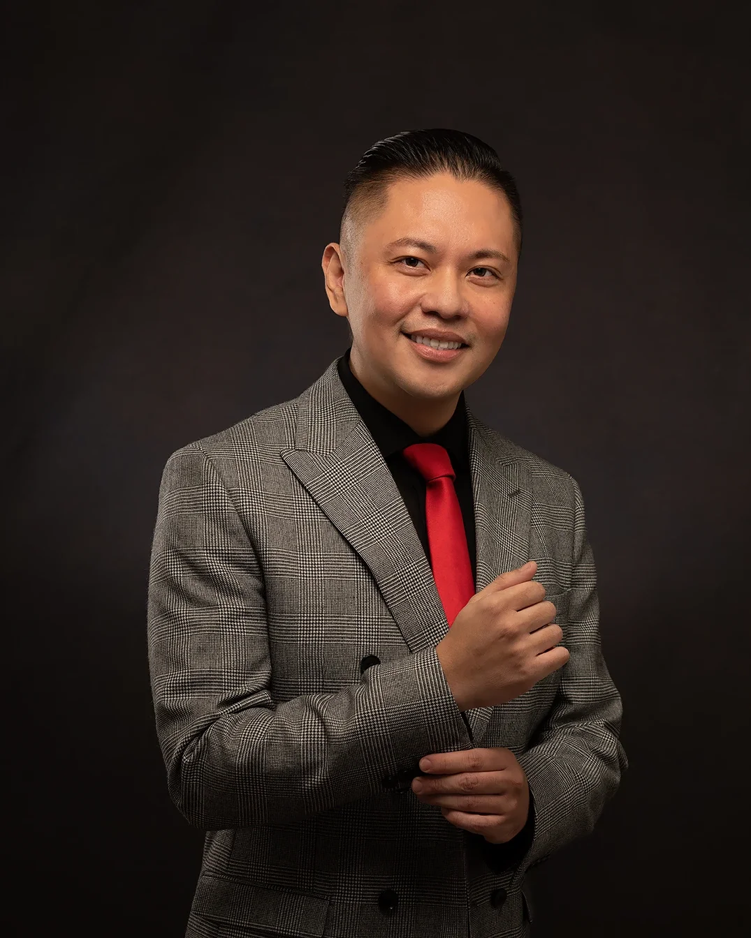 Professional male business headshot in a gray suit and red tie photographed on a dark studio background in Los Angeles.