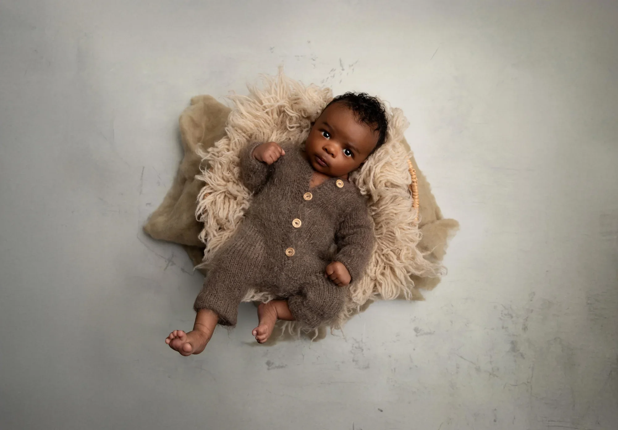 Newborn baby in a neutral brown outfit photographed in a cozy basket during a professional newborn photography session in Los Angeles.