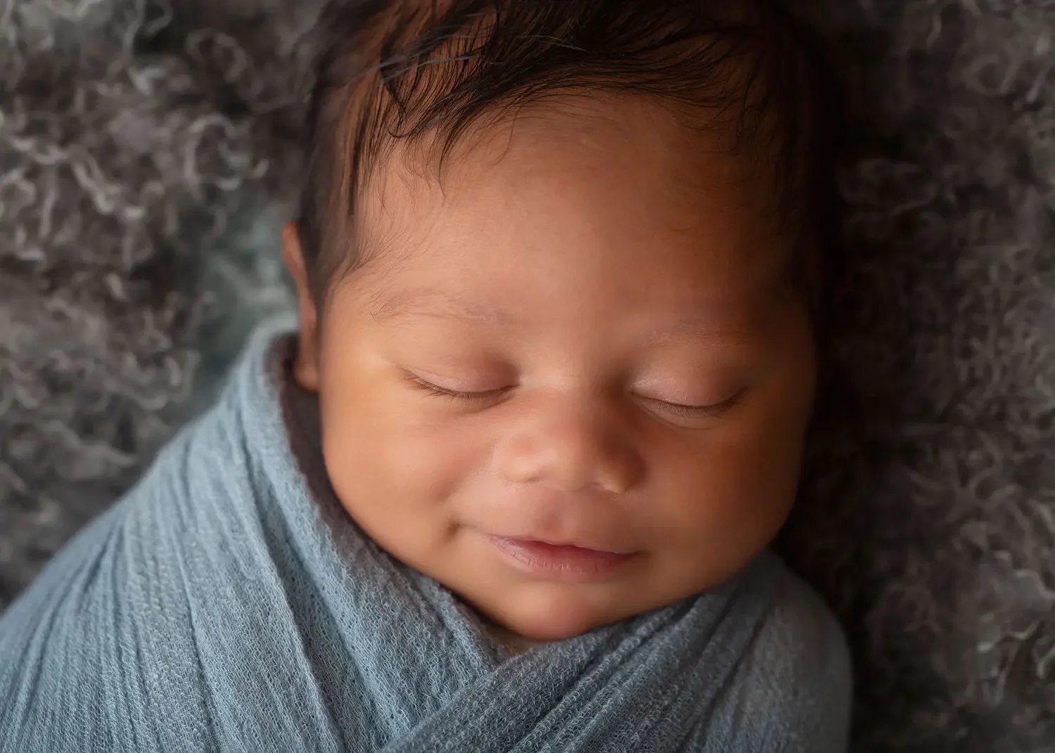 Close-up of a sleeping baby wrapped in a blue blanket, lying on a textured grey surface in a Los Angeles Newborn Photographer studio..