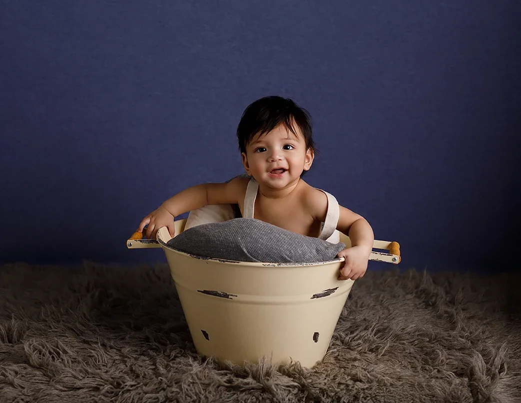 Six-month-old baby smiling in a cream-colored bucket during a milestone photography session in Los Angeles.