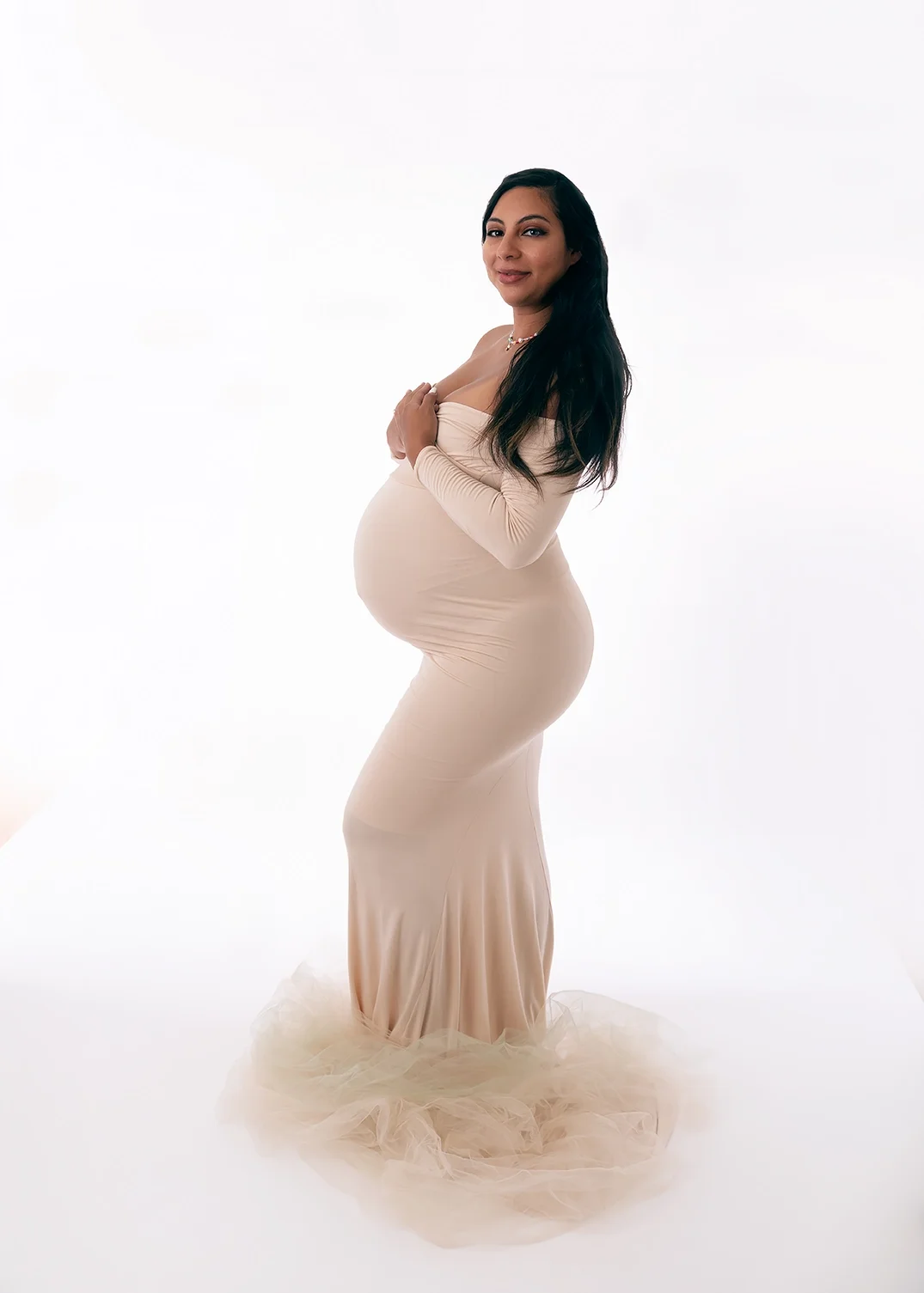 Expecting mother in a fitted cream maternity gown posed in profile during a studio maternity photography session in Los Angeles.