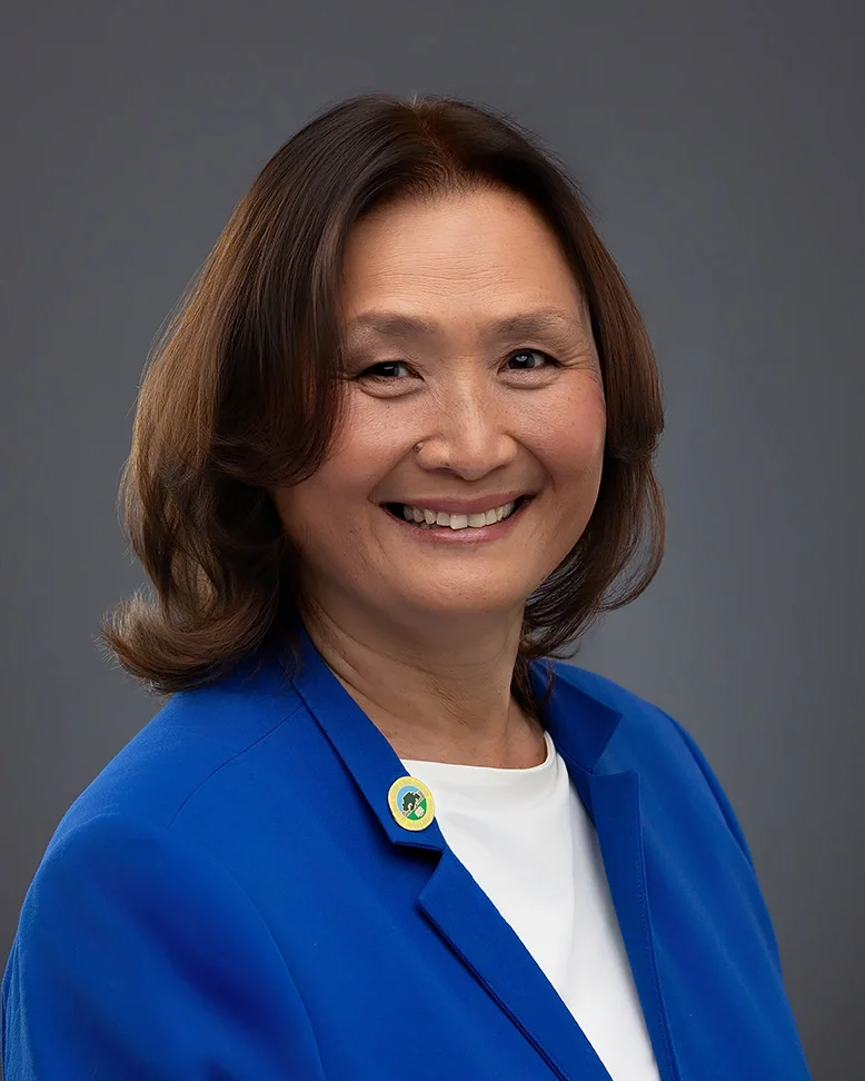 Professional business headshot of a woman in a blue blazer photographed against a clean gray studio background. The polished lighting and approachable expression create a professional portrait suitable for executive profiles, company websites, Linked