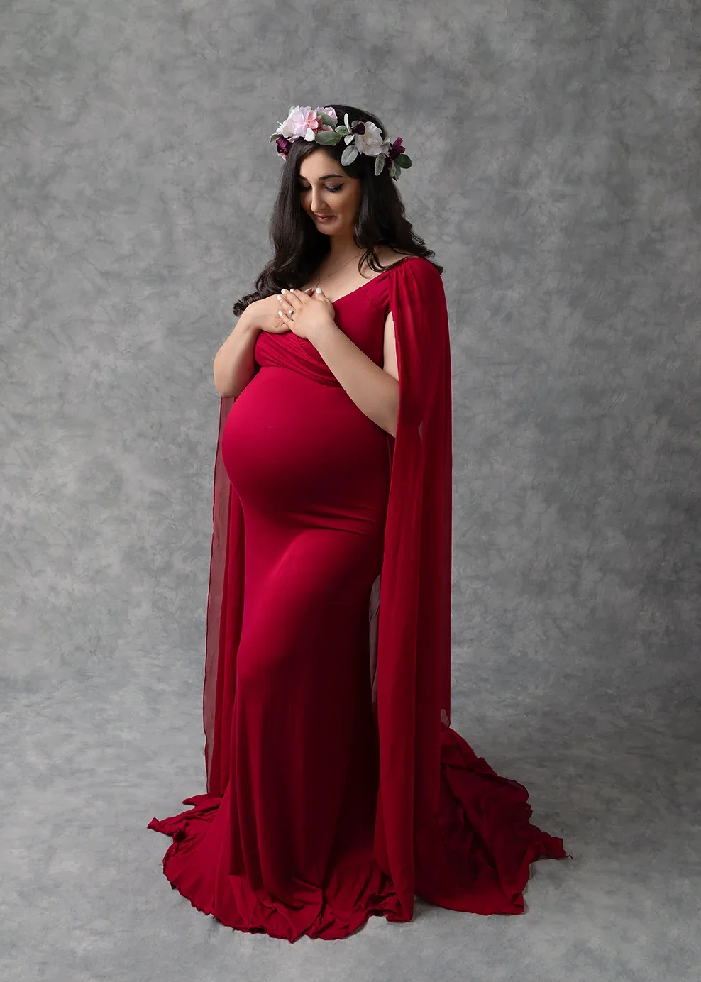 Expecting mother in a fitted red maternity gown and floral crown posing for a studio maternity portrait in Los Angeles.