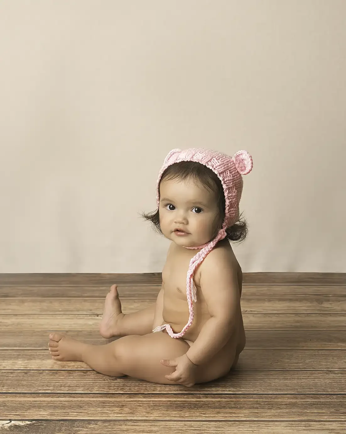 Sitting baby wearing a pink knit bonnet during a milestone photography session in Los Angeles.