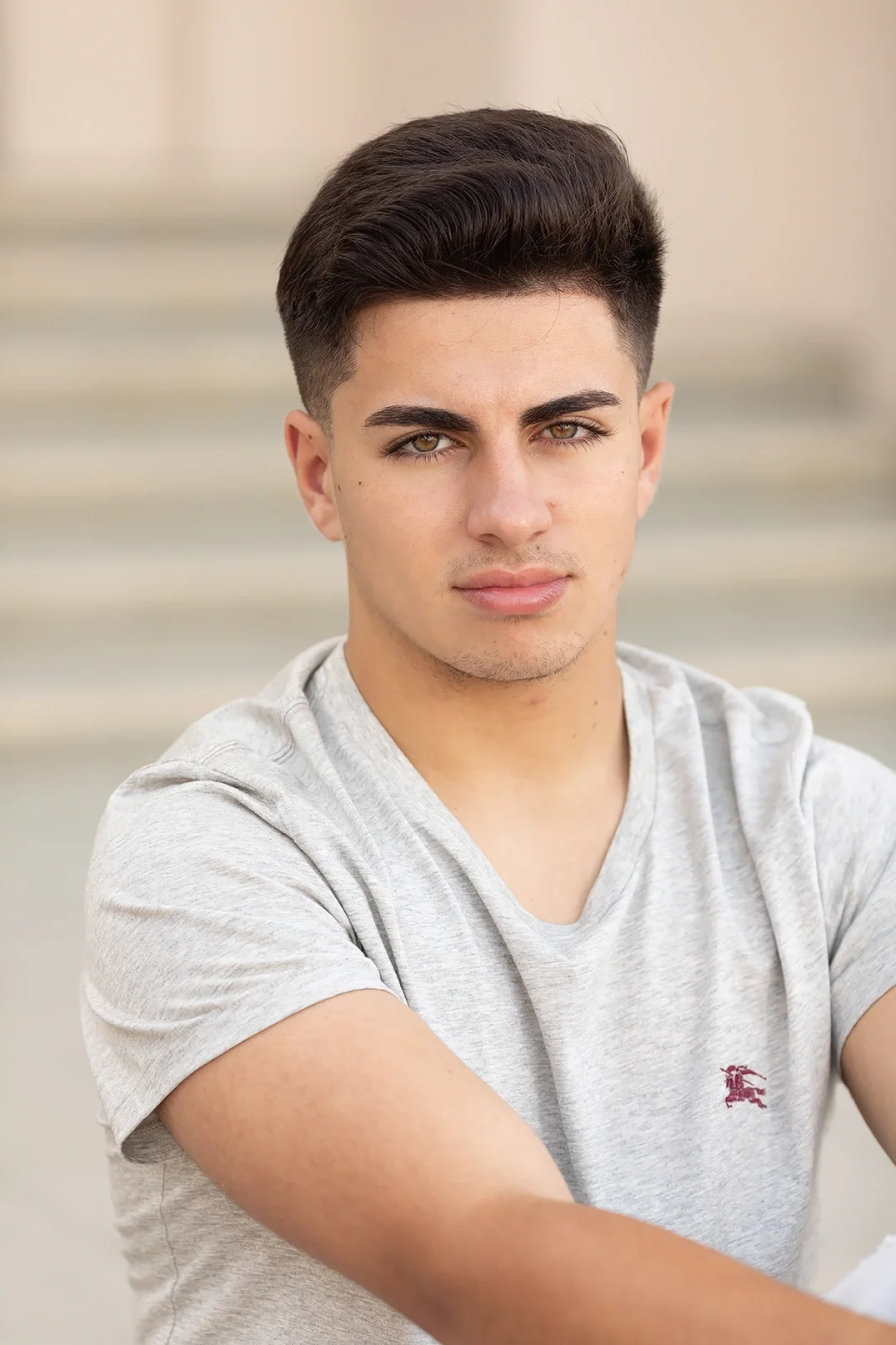 Actor headshot of a young man photographed outdoors with soft natural light and a neutral background. The close composition and direct expression create a clean, contemporary portrait suitable for acting submissions, casting profiles, and professiona