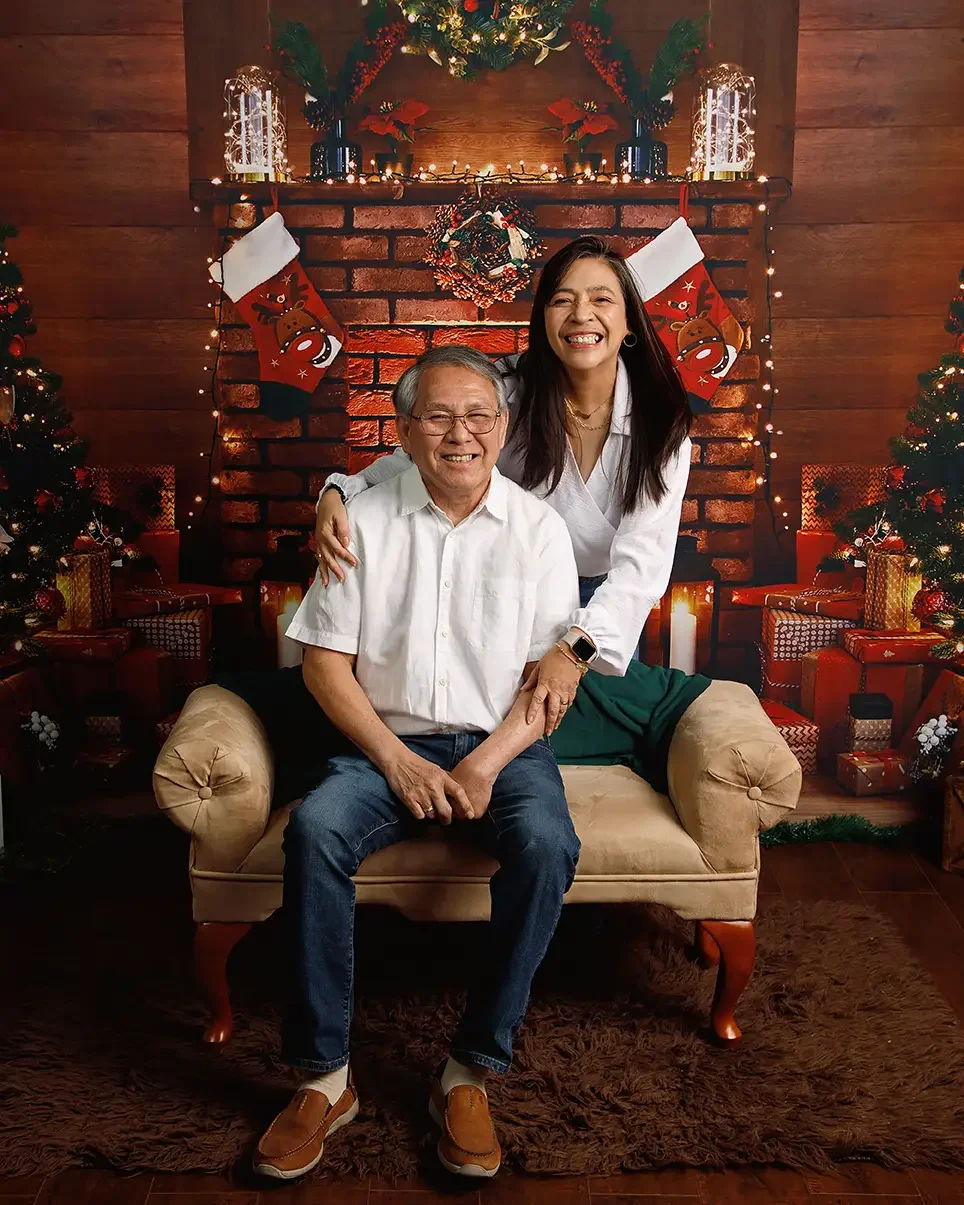 Couple wearing eyeglasses during a professionally lit family holiday portrait in front of a Christmas fireplace. Studio lighting minimizes reflections on glasses for flattering family Christmas photos