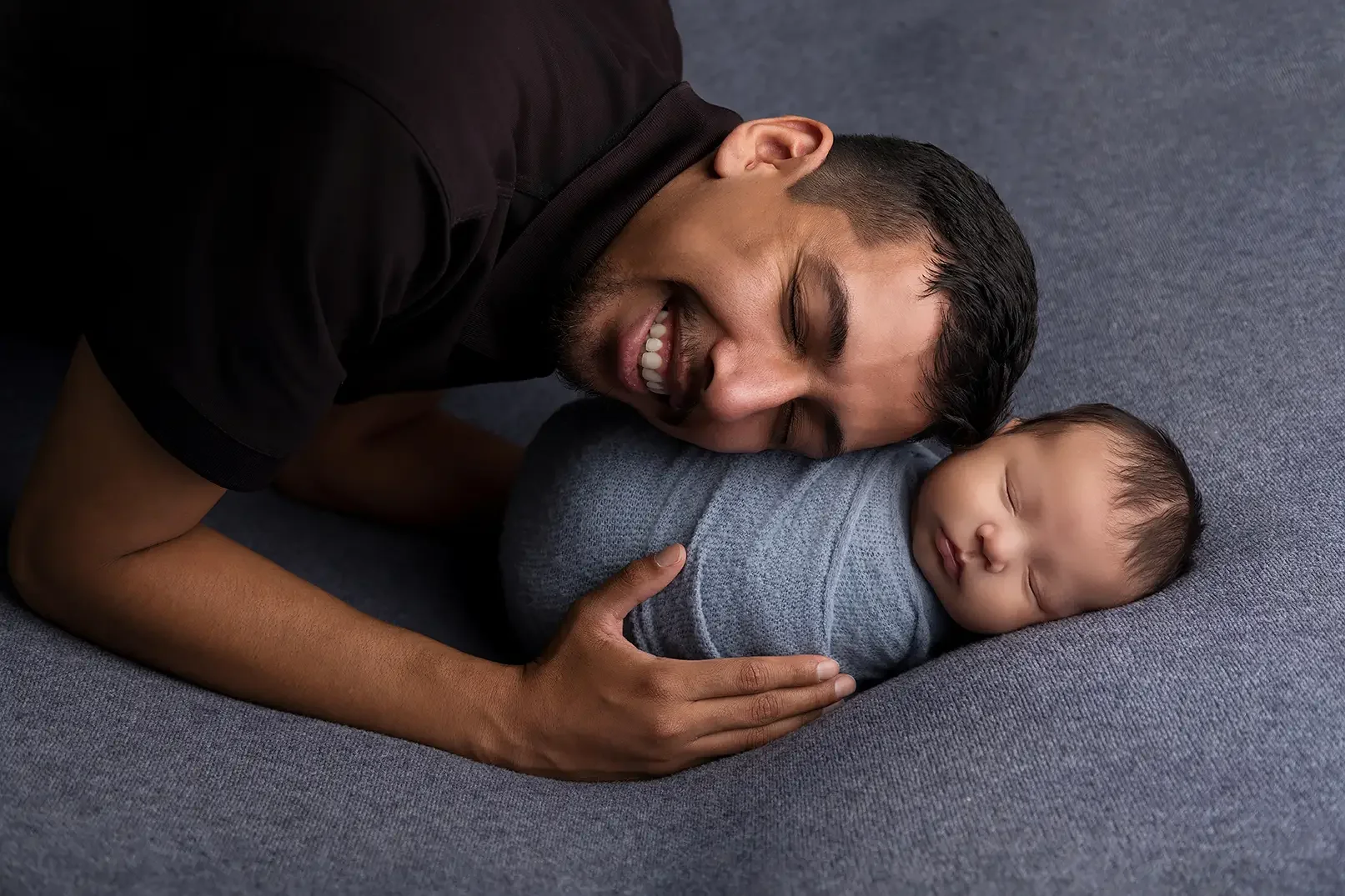 Father smiling beside his sleeping newborn baby during a Los Angeles newborn photography session.