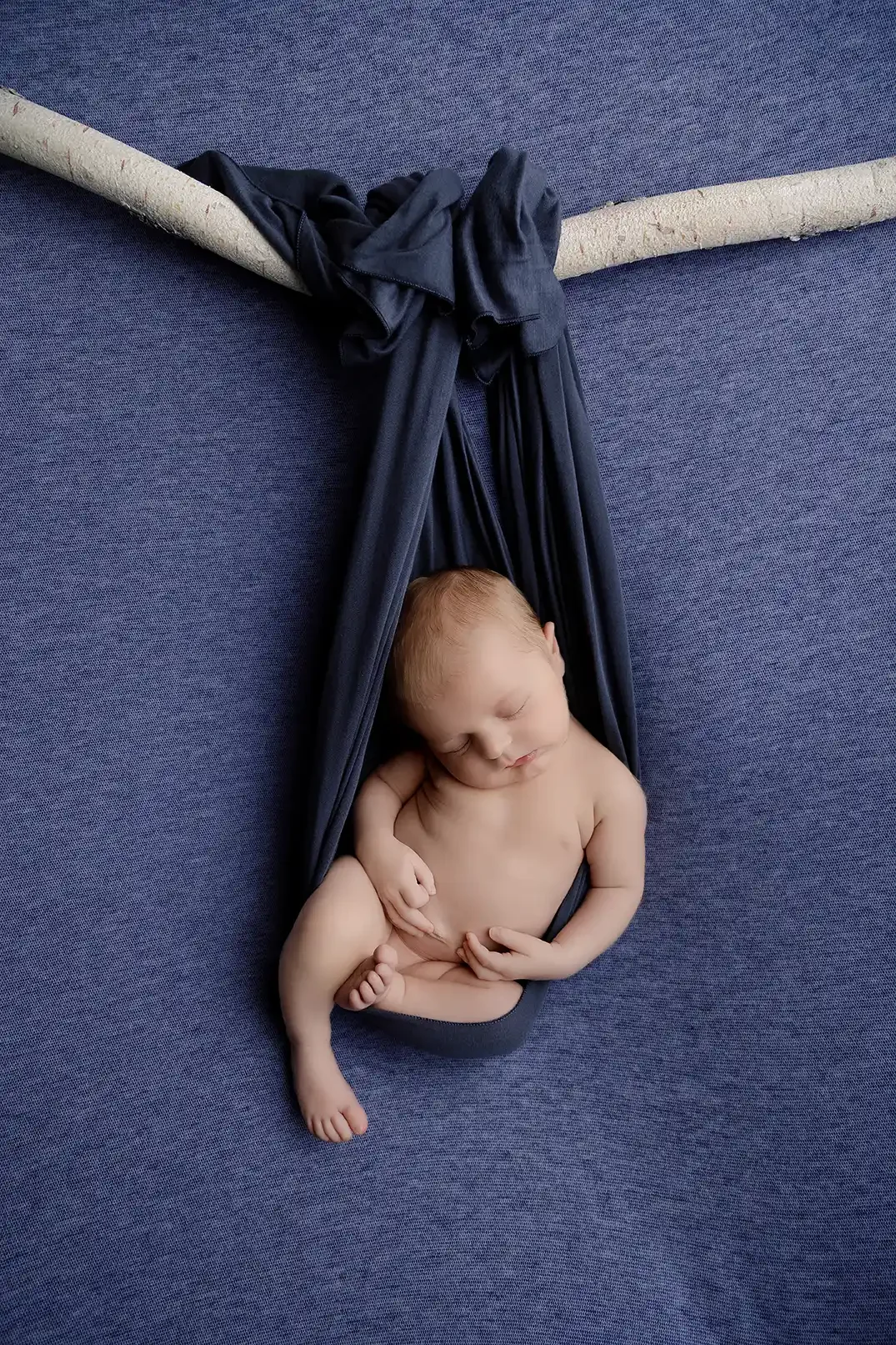 Sleeping newborn baby posed in dark blue fabric during a professional newborn photography session in Los Angeles.