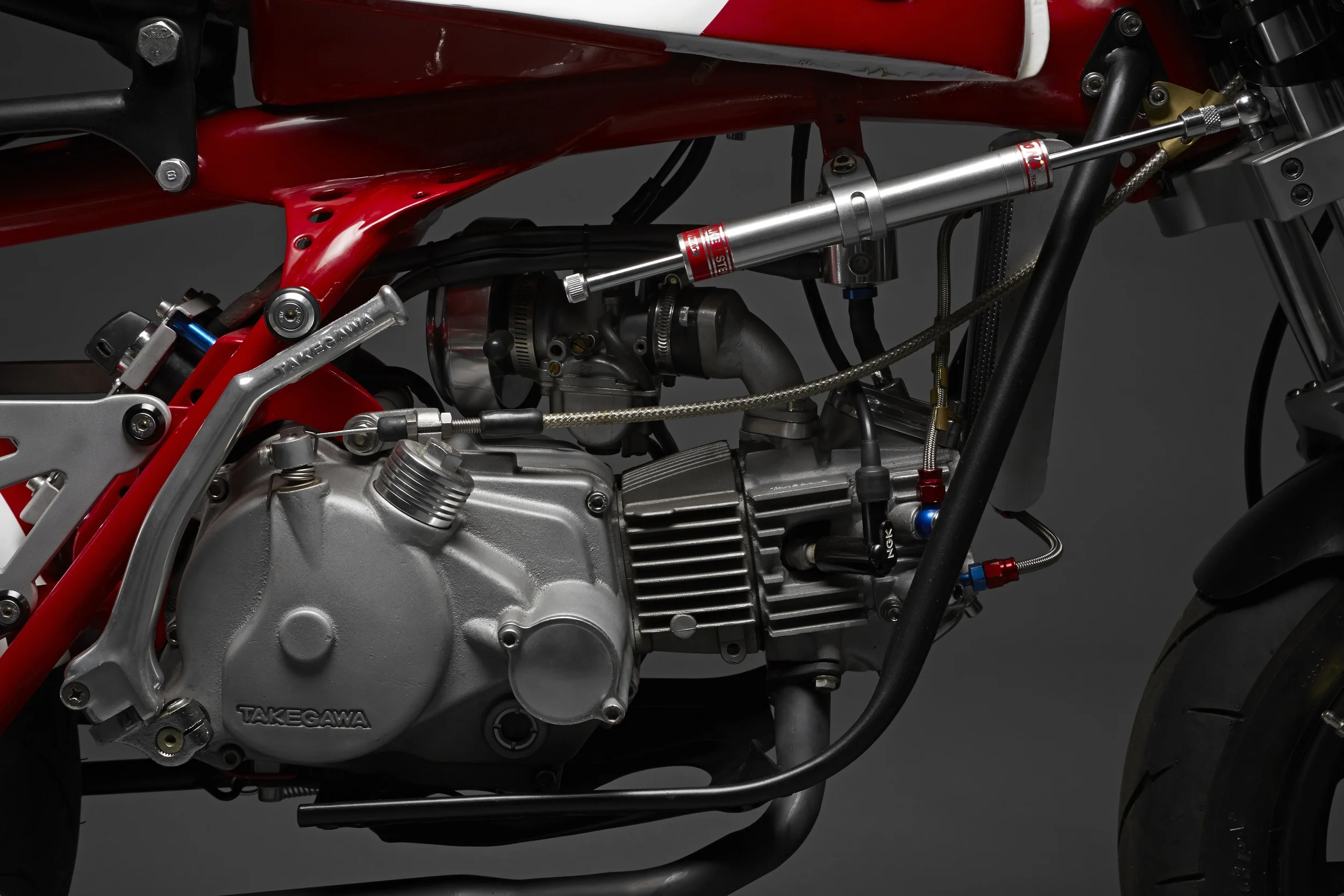 Takegawa 4-valve head, race cam, cylinder, piston, stroker crank, high volume oil pump, street outer rotor ignition/lighting stator, Hyper CDI, Special Clutch, 5 speed tranny, kickstarter, and magneto cover. A modified Honda CT90 brush guard was used to make the engine cradle.