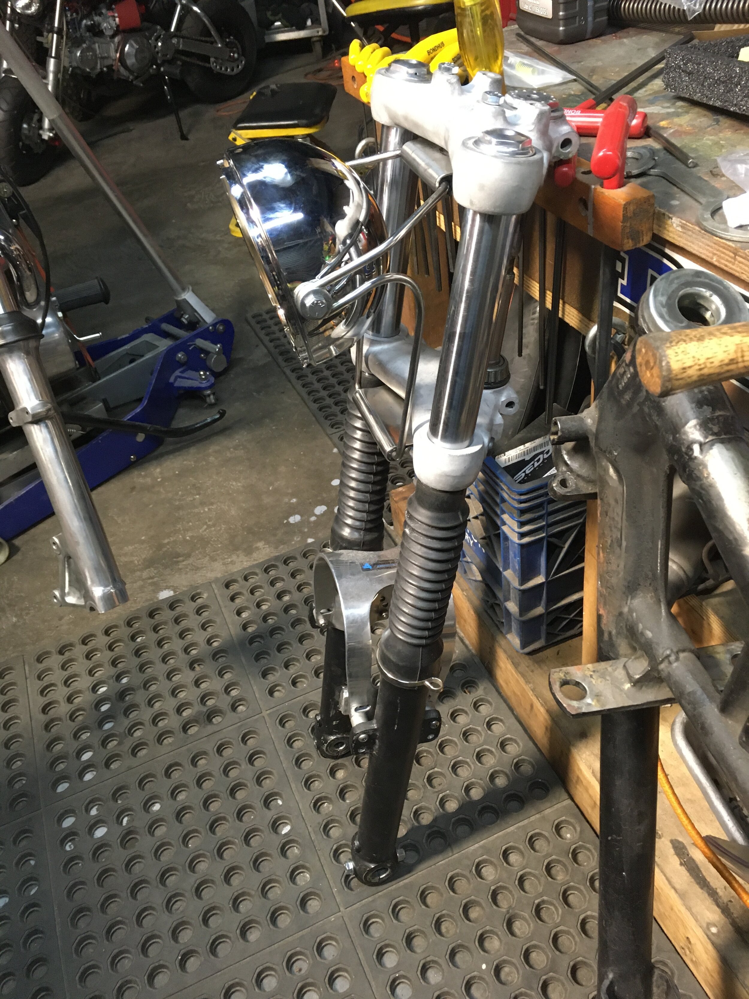  Ceriani triple trees and forks with a custom headlight mount. The bucket is a Lucas 5 3/4” unit. The fork brace is a Cal-Customs NOS piece. 