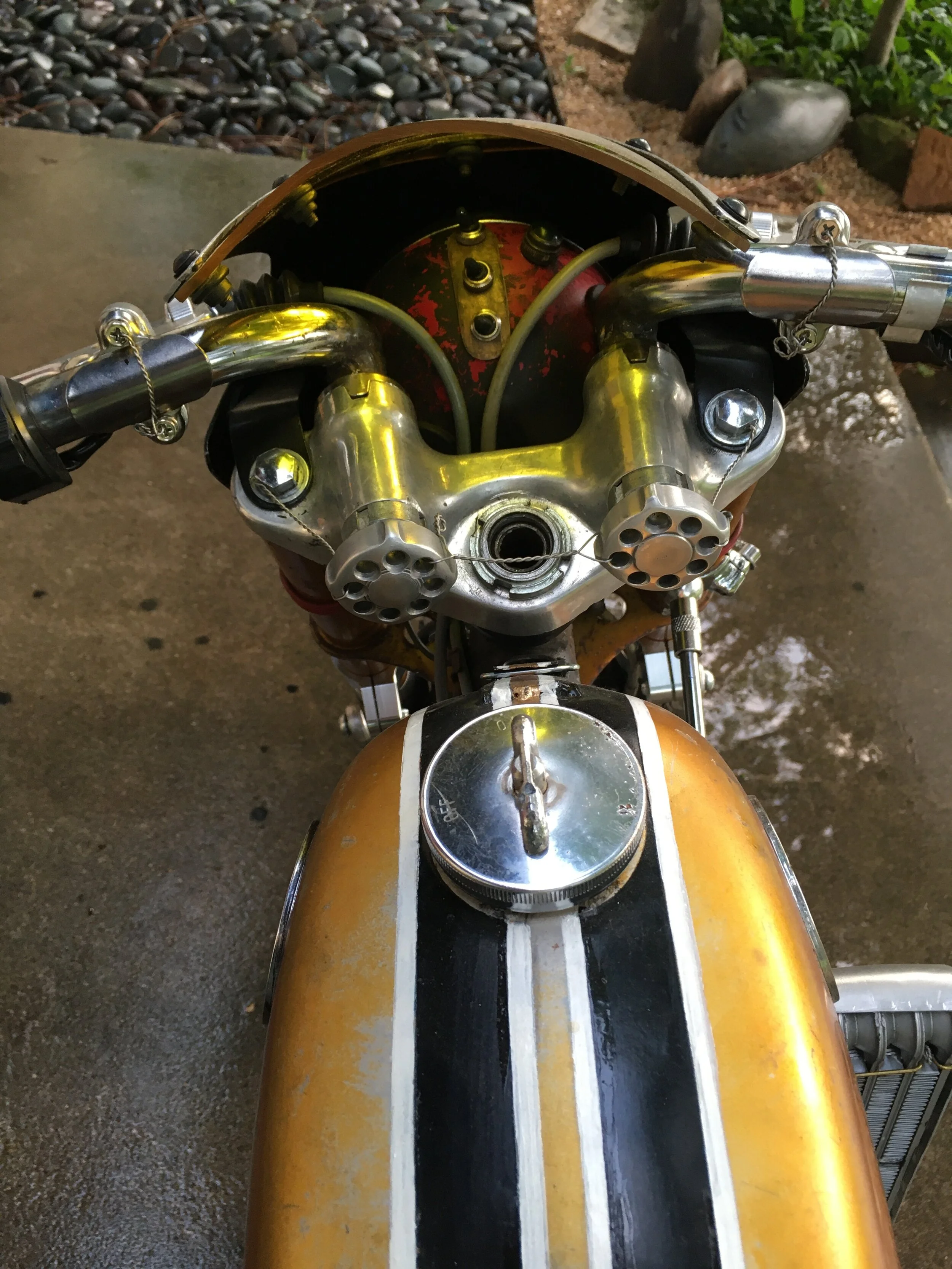  In order to use the early model tripletree clamp with its shorter steering tube, a special nut was turned that recesses in the clamp. Custom aluminum clamping knobs keep it all tight together. Much of the hardware is safety-wired. An SL70 headlight 