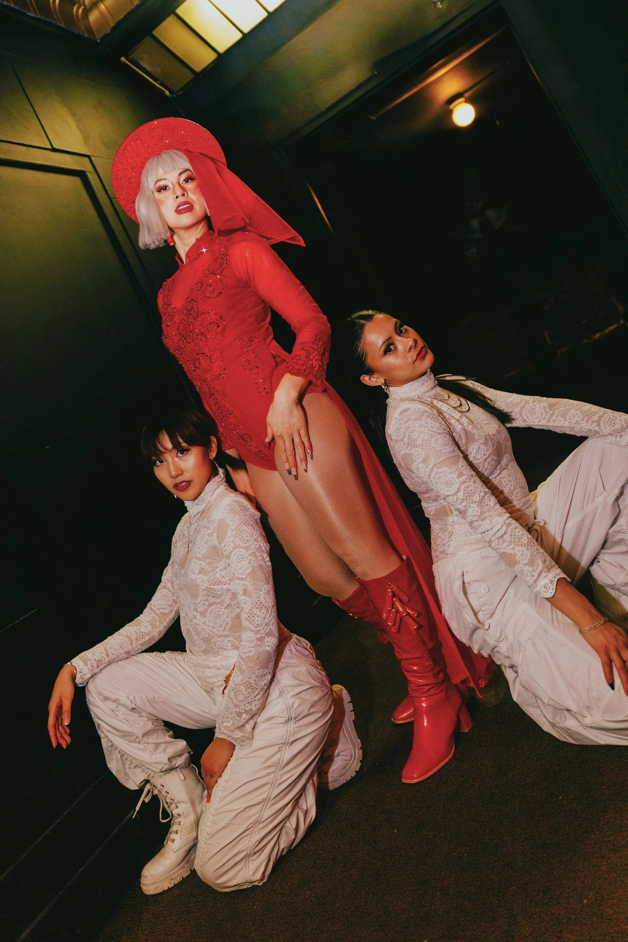 promqueen (musician) dressed in red vietnamese traditional attire posing with two dancers dressed in white