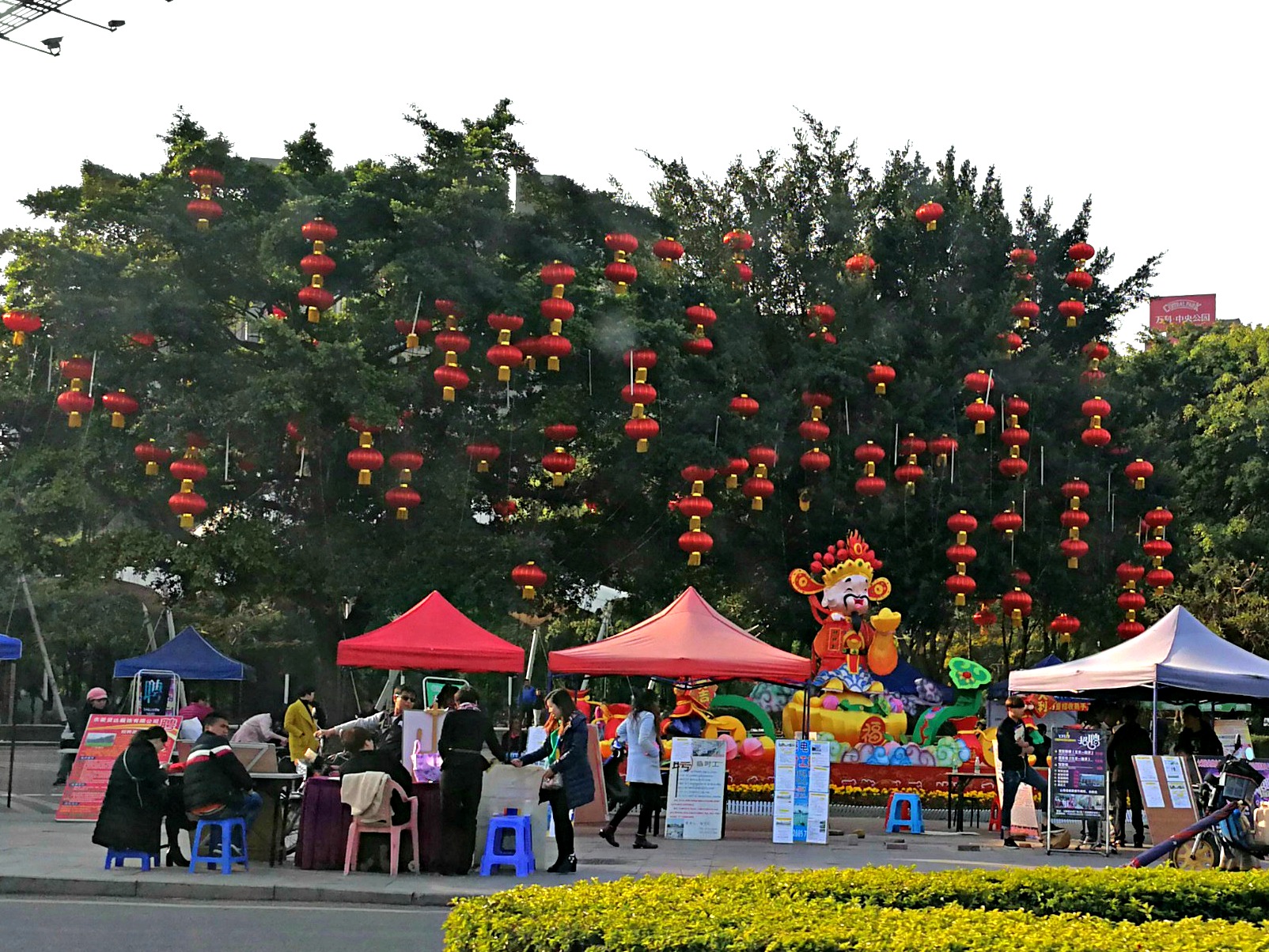 This picture shows both smaller red lanterns in the trees, and a large silk decorative lantern of the God of Wealth, which seems appropriate as this is the area where the job fair is held!
