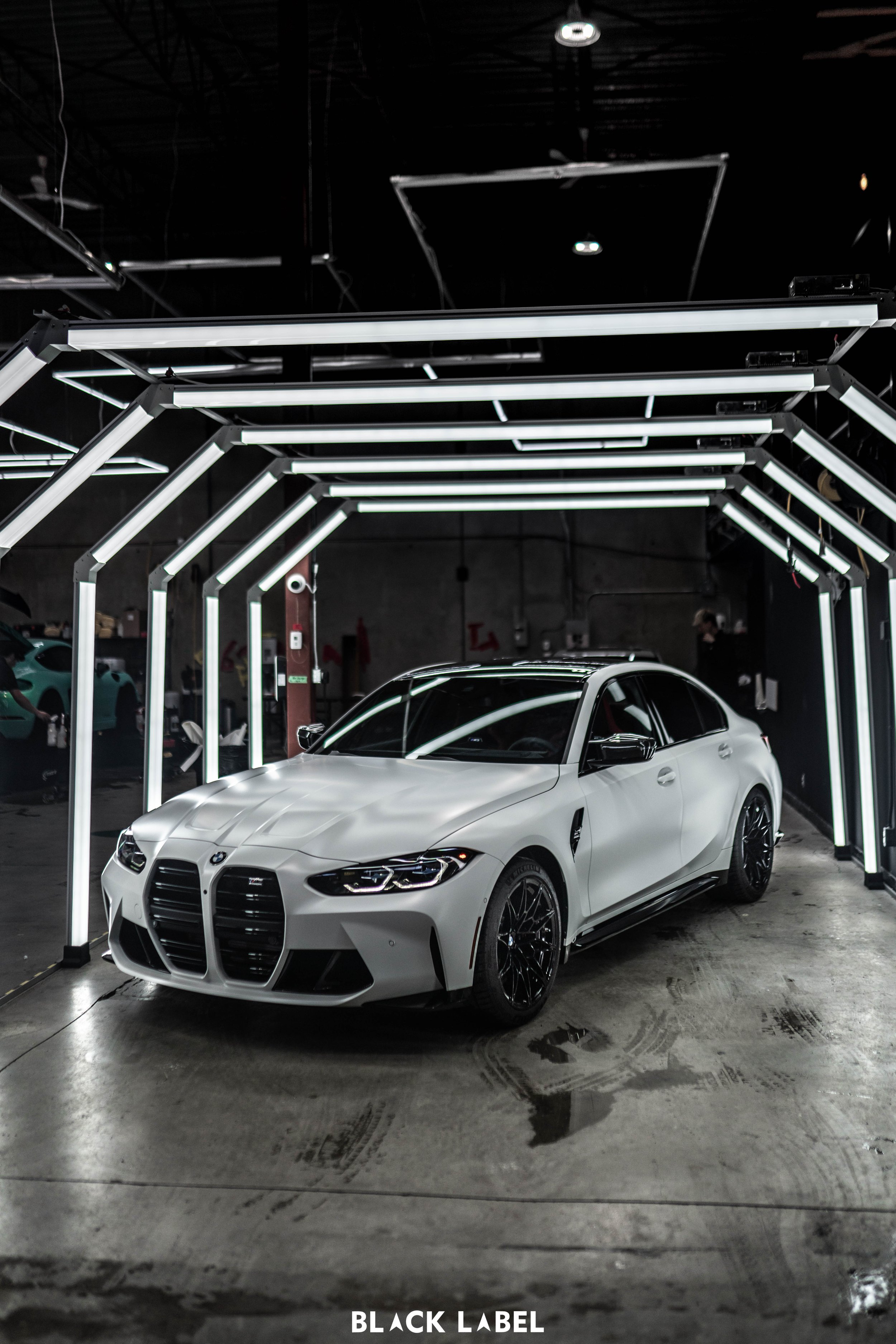 White BMW M3 sports car parked inside a modern garage with bright white LED strip lighting installation overhead.