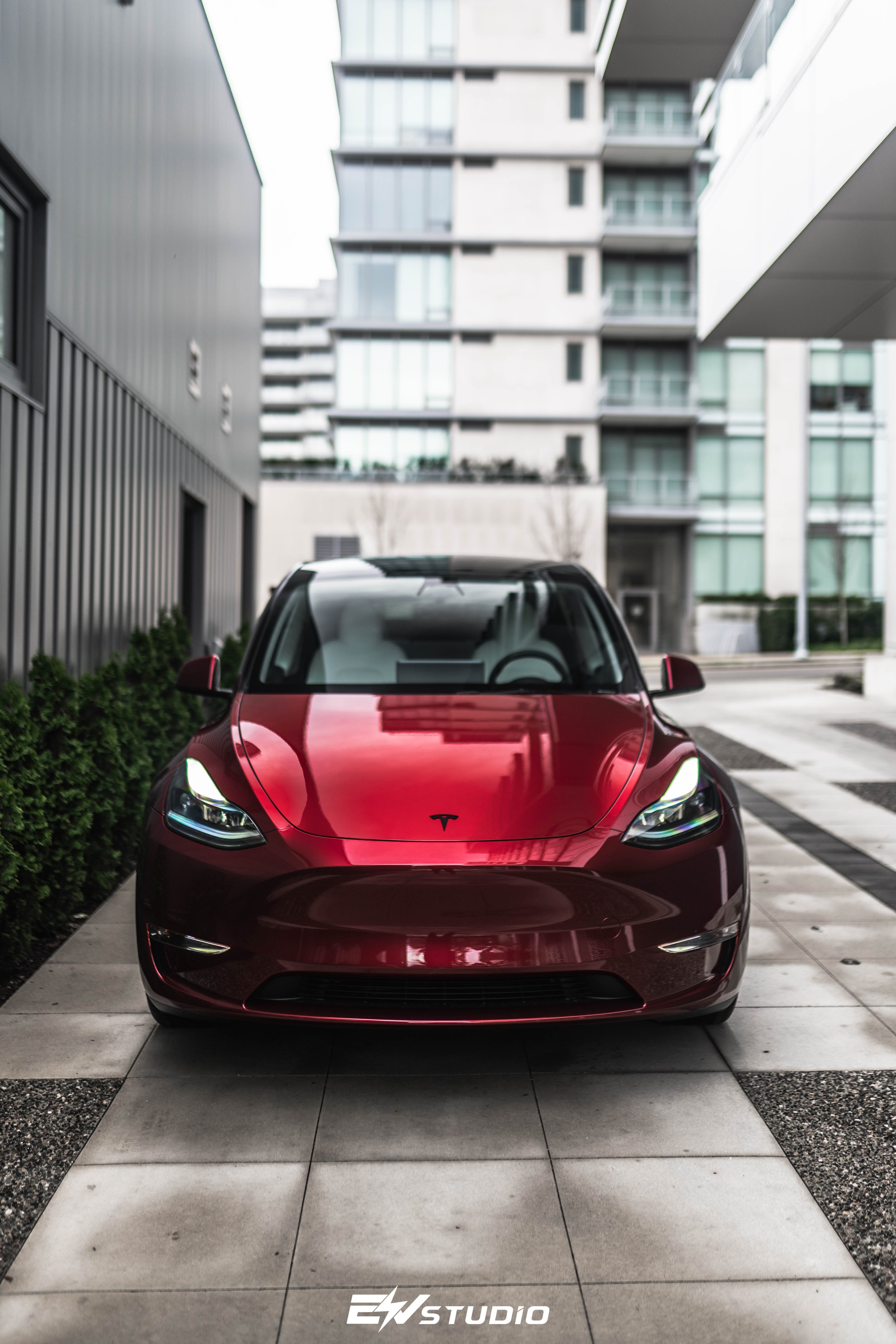 Red Tesla Model 3 parked in a modern urban setting with high-rise buildings in the background.
