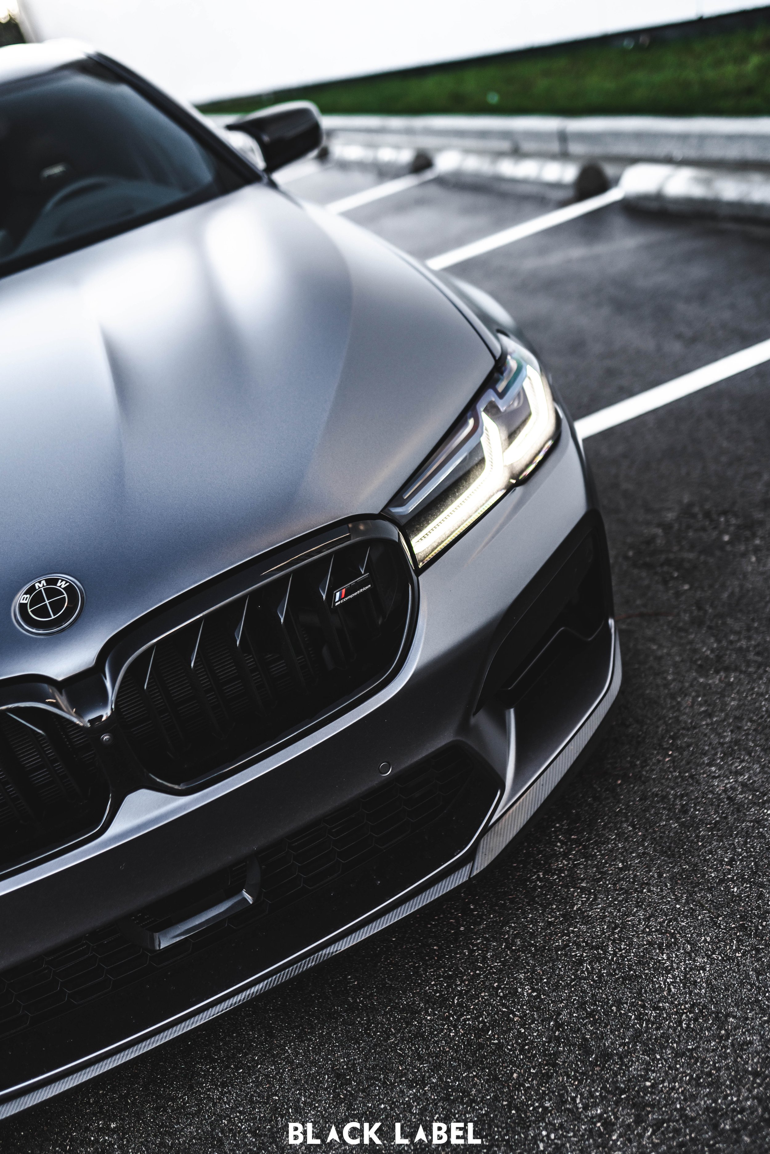 Close-up of the front of a silver BMW car in a parking lot, showing the grille, headlights, and hood, with the BMW logo visible.