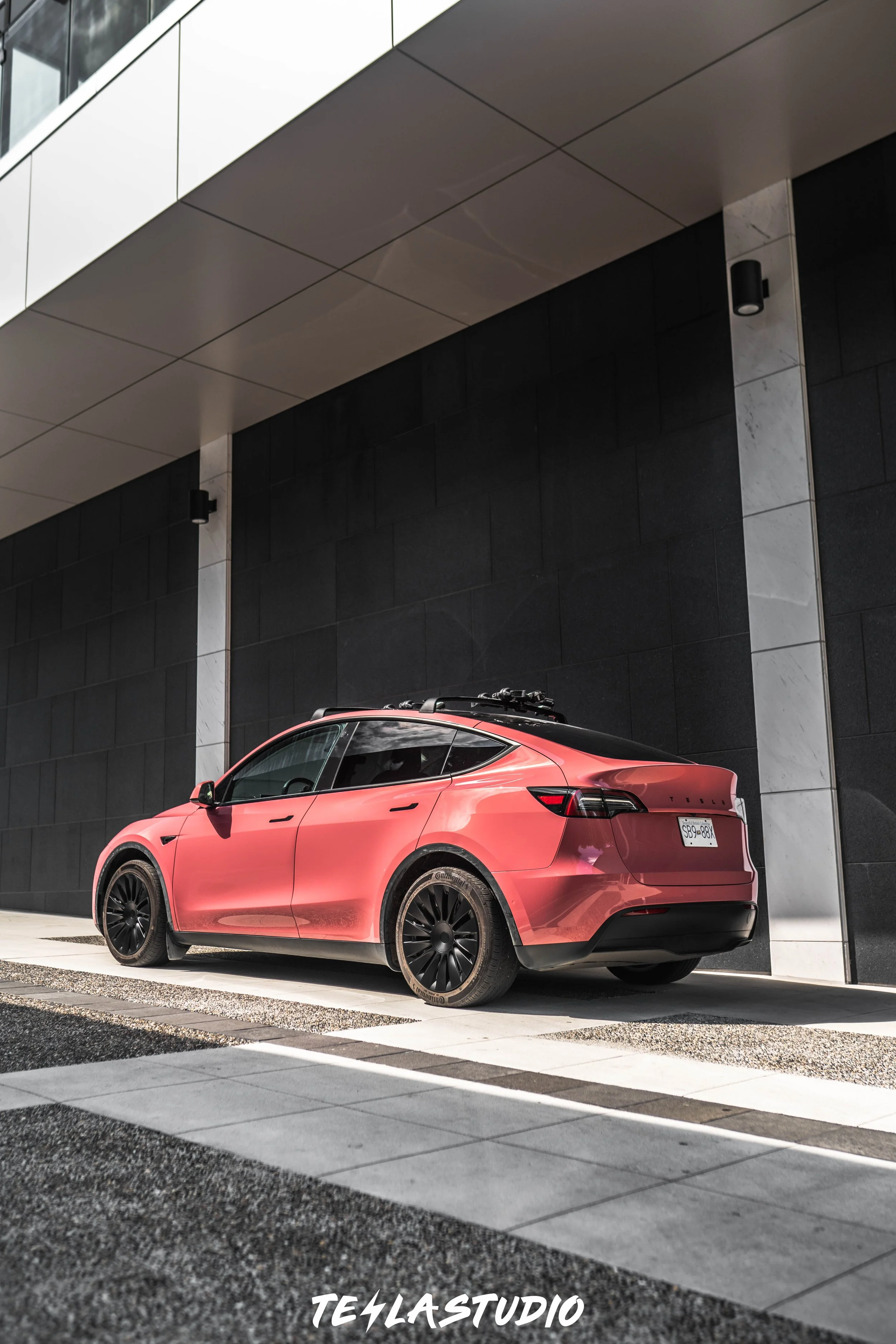 A red electric car parked on a sidewalk beside a modern building with black and white panels.