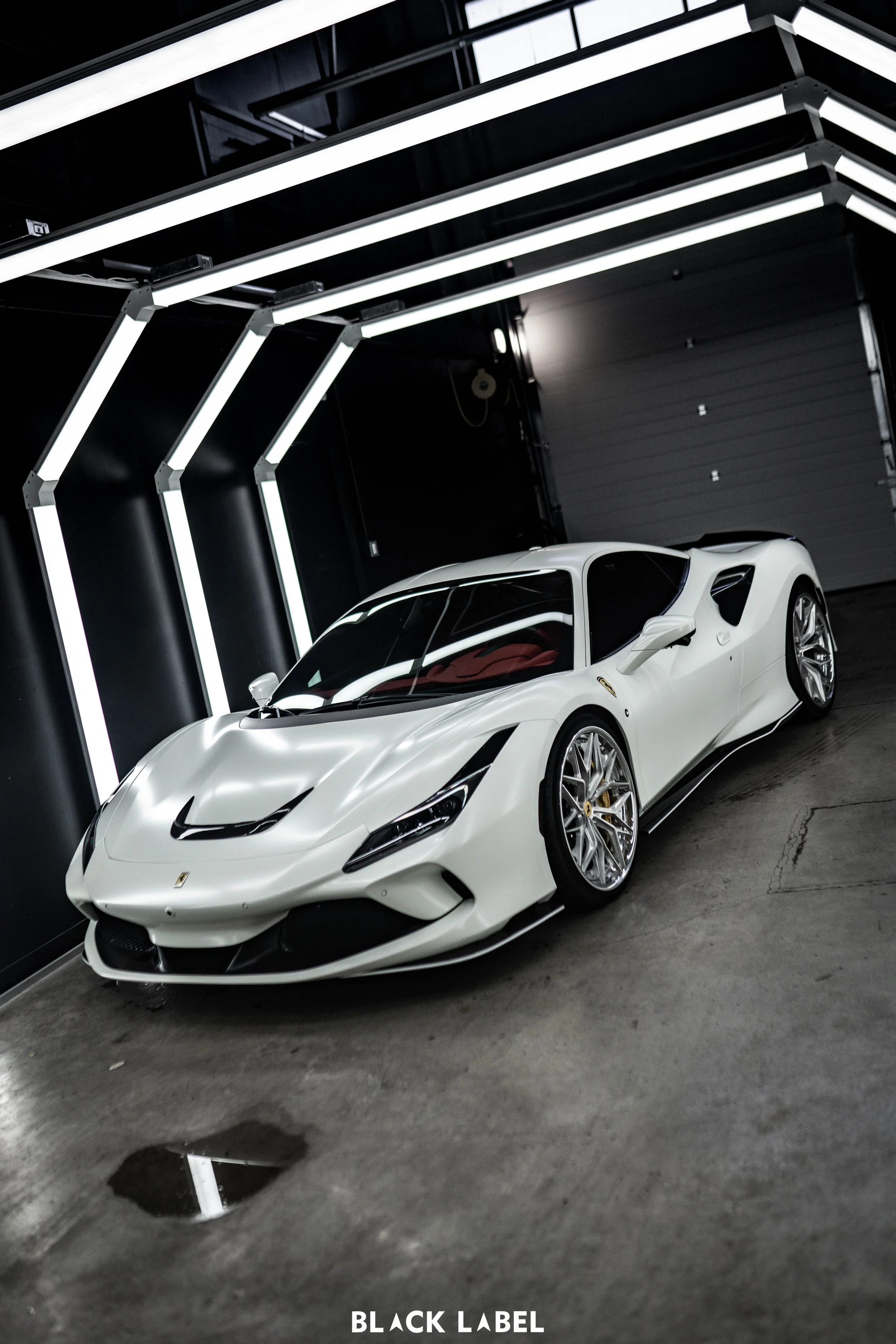A white sports car, likely a Ferrari, parked inside a modern garage with black walls and bright LED strip lights overhead.