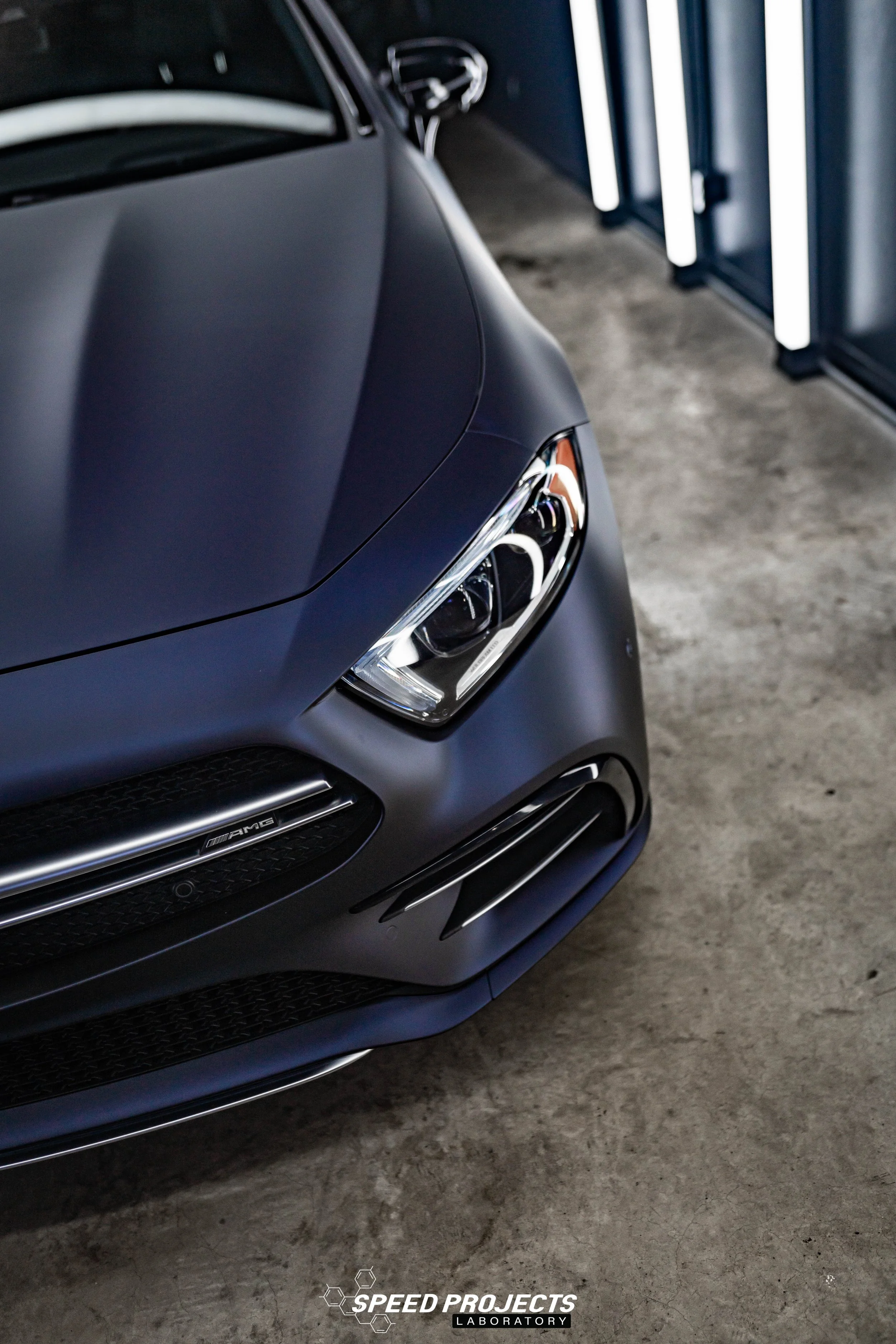 Close-up of the front of a matte black Mercedes-Benz AMG car in a garage with a concrete floor.