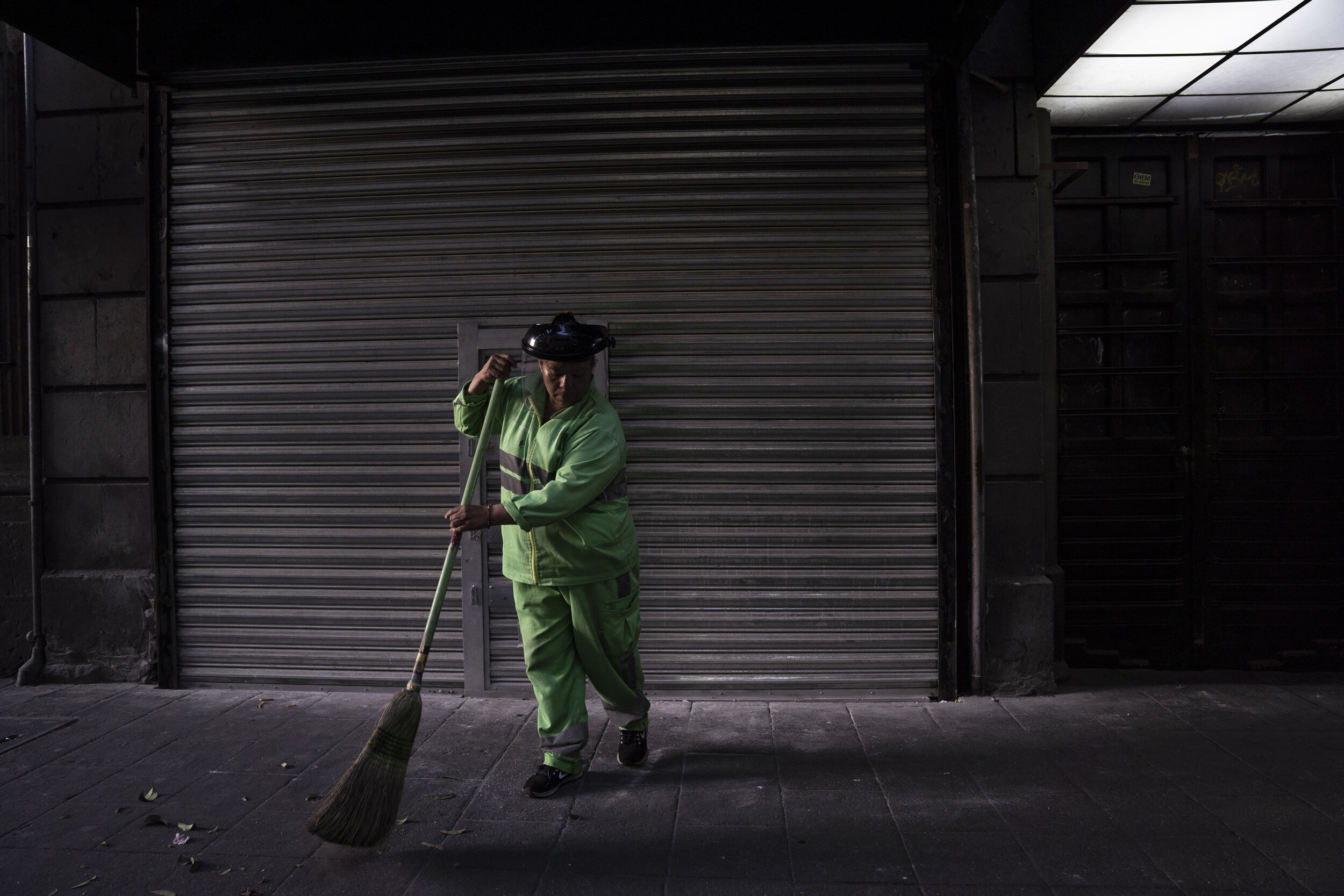   A worker sweeps the sidewalk wearing a protective mask during phase two of contingency measures, Mexico City.  