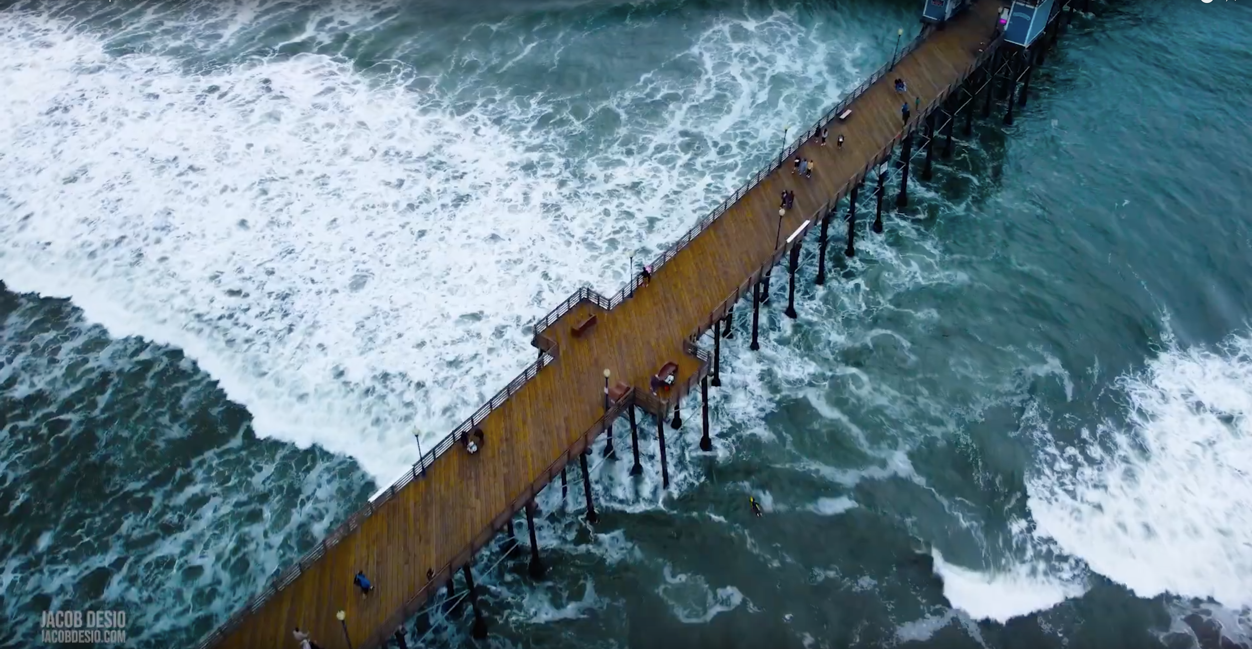 overhead drone shot of pier over ocean waves.png
