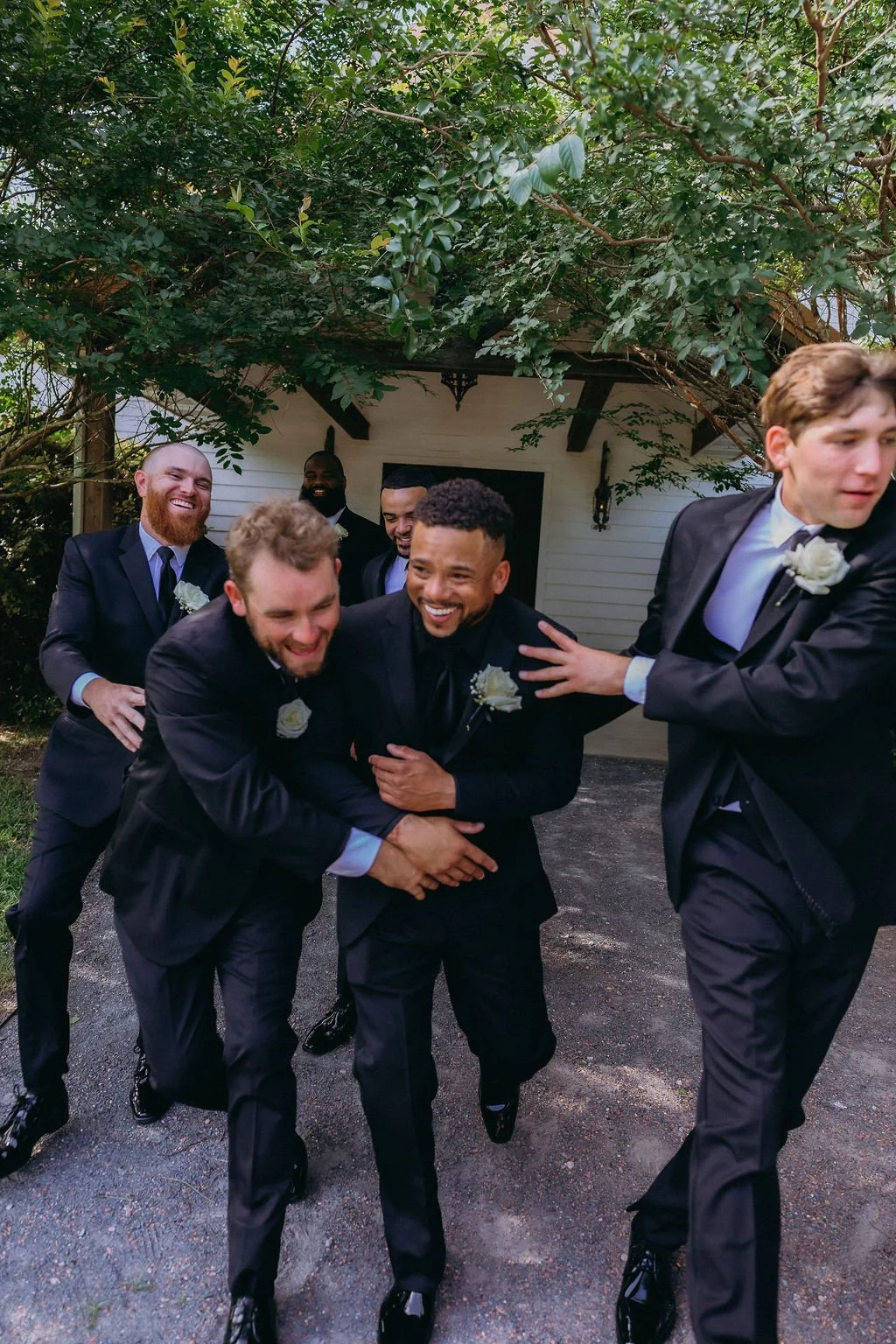 11-groom-and-groomsmen-in-black-tuxedos-laughing-outside-the-stone-barn-at.jpg