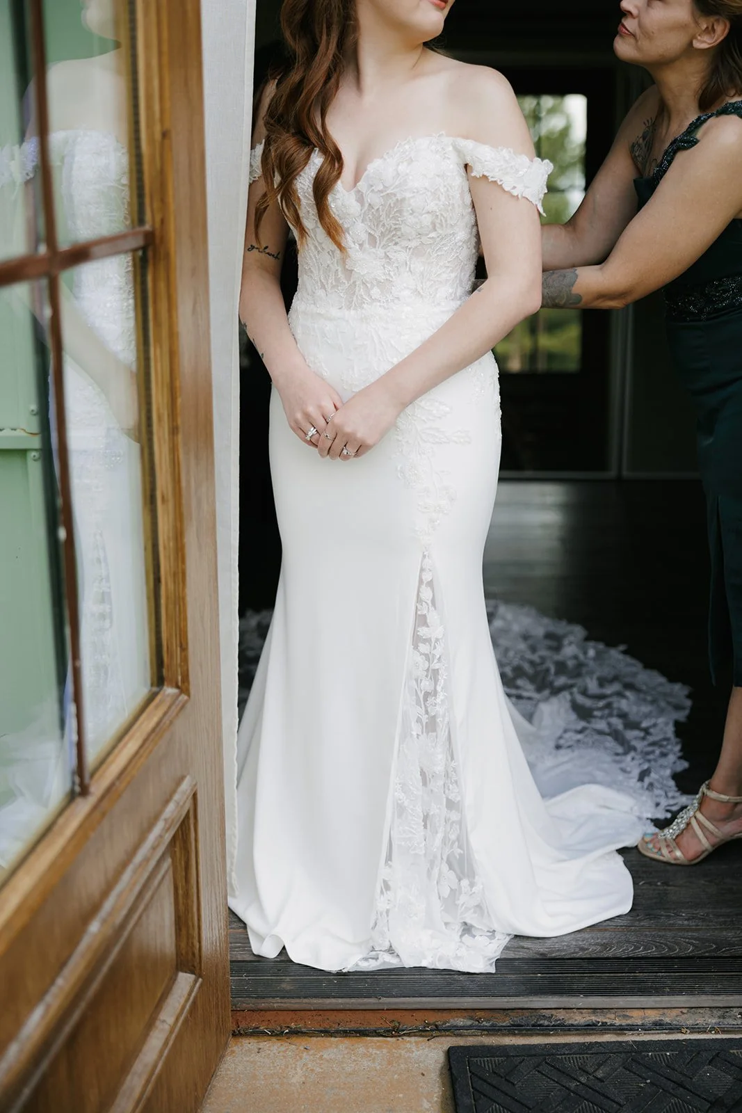 06-bride-in-an-off-the-shoulder-lace-gown-being-helped-into-her-dress-at.jpg