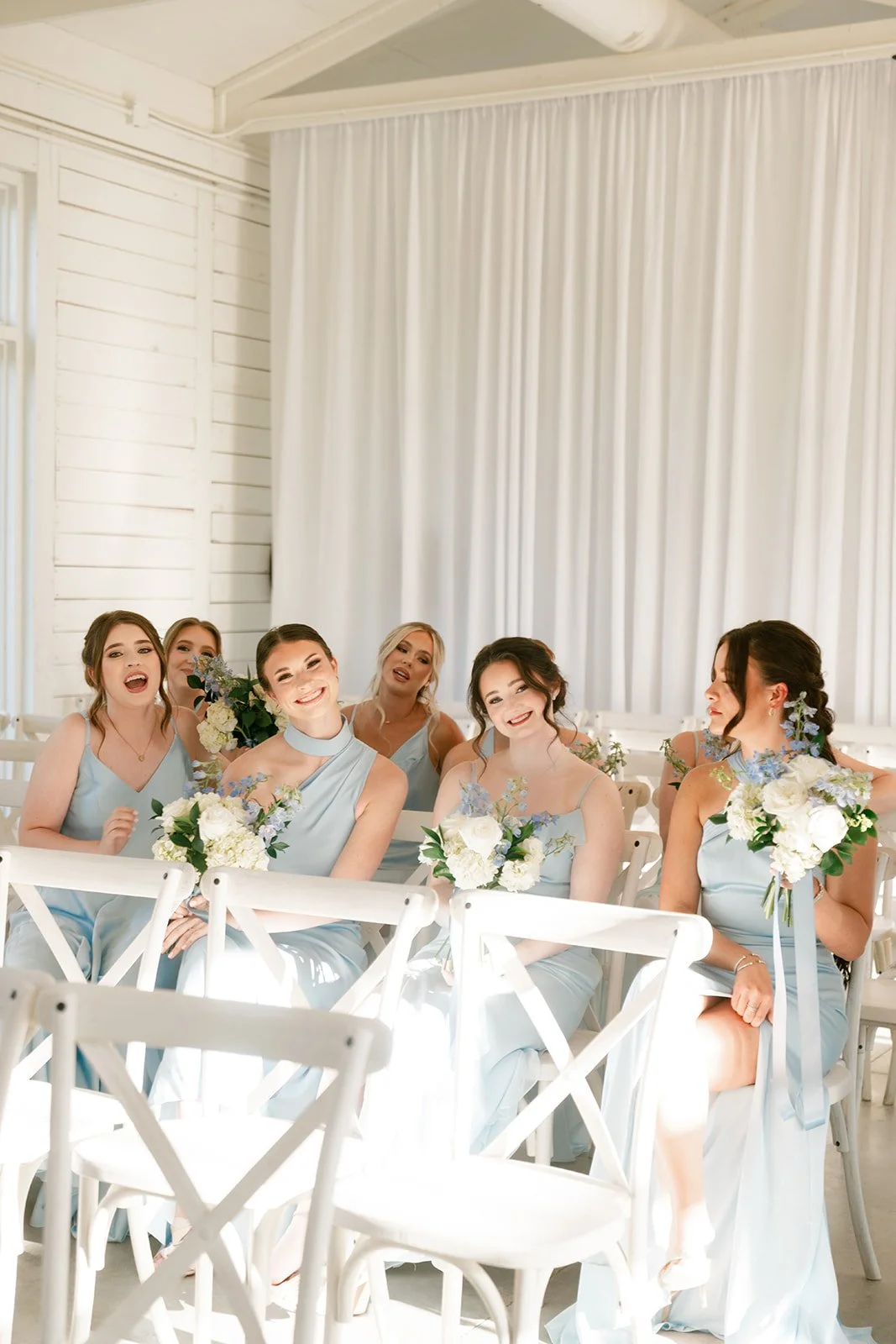 08-bridesmaids-in-sky-blue-waiting-on-white-cross-back-chairs-in-the.jpg