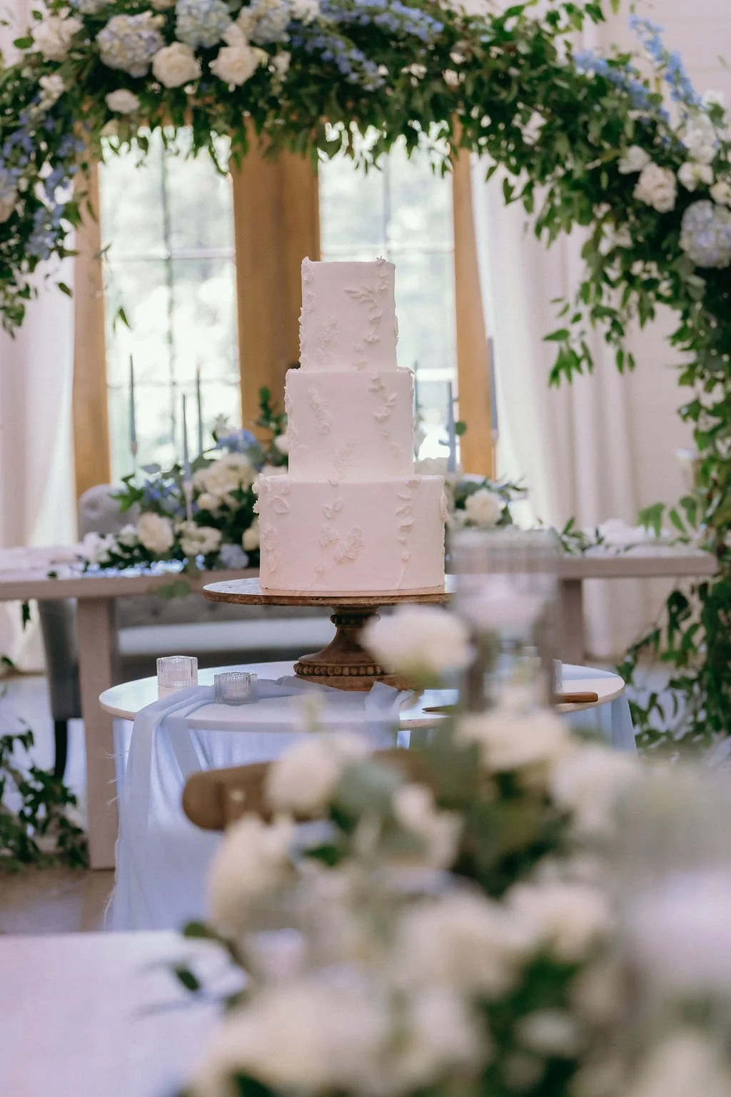 34-three-tier-white-wedding-cake-beneath-a-floral-arch-at-the-stone-barn.jpg