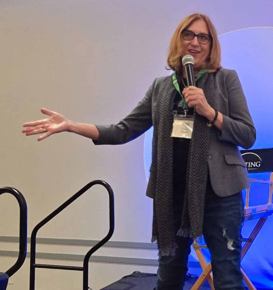 Debra Ann Mumm speaking on stage with a microphone during a keynote presentation.