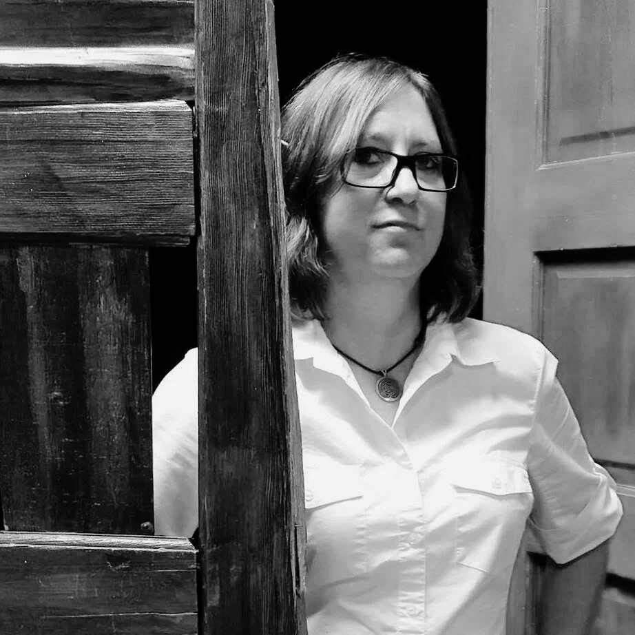 Black and white portrait of Debra Ann Mumm standing in a doorway, looking calmly toward the camera.