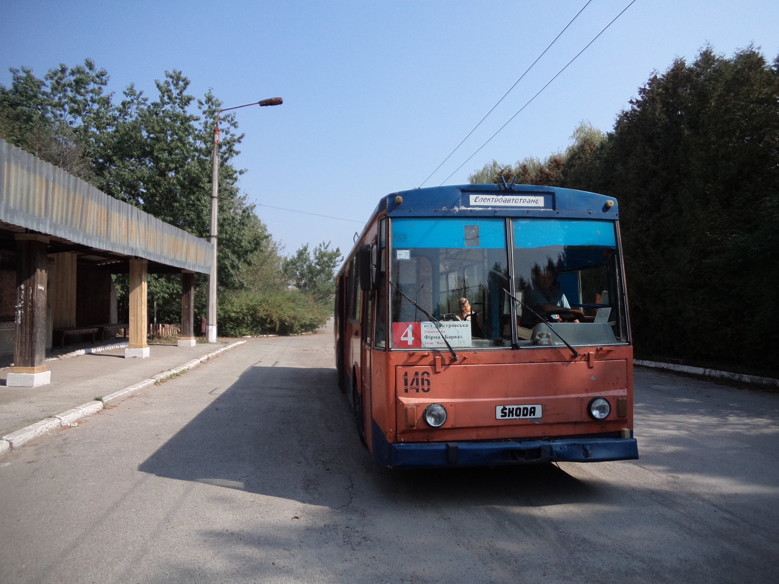 Konečná zastávka Firma Barva v detailu. Trať vedená do těchto míst byla otevřena v roce 1989 a přinejmenším její koncový úsek má své nejlepší časy za sebou. Zřejmě jen díky tomu, že trolejbusy obsluhují po trase nedalekou vesnici Jamnycja, u které se mimochodem nachází jedna z největších a nejmodernějších cementáren Ukrajiny, přežívá trolej nad silnicí H09 do dnešních dnů. Na snímku zobrazený vůz ev. č. 146 patří do série vozů t ypu 14Tr02/6 pořízené na konci 80. let a vedené pod ev. č. 141 –156. V současnosti nezasahuje z 16 vozidel do provozu jen jedno, ev. č. 145, jež je už postupně likvidováno. 