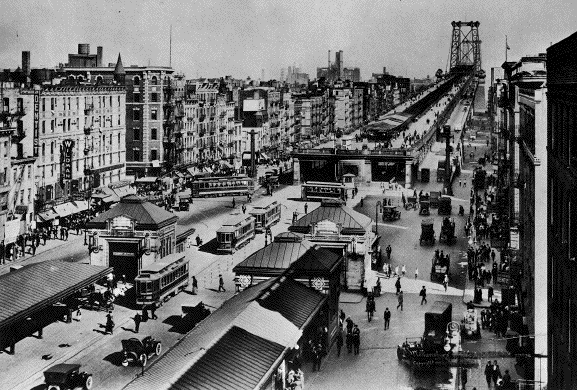 Dopravní ruch u mostu Williamsburg Bridge v roce 1919. Na povrchu vidíme tramvaje společností zajišťujících dopravu na Manhattanu. Do Williamsburgu (Brooklynu) však některé přejížděly, byť jen hned za most. Kdo toužil jet dále do nitra Brooklynu, mohl vystoupit na některé ze zastávek na povrchu a zamířit k výrazným kamenným kioskům, které ukrývaly schody do podzemí. Těmi bylo možné dostat se k tramvajím společnosti BRT i k metru. (zdroj: Wikipedia.org)