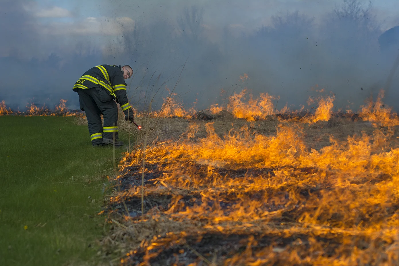 A firefighter from the Kent Fire Department uses a road flare to light the prairie grass behind the Student Recreation and Wellness Center on April 28, 2015. The controlled prairie fire is done annually by the department to naturally control the growth of the prairie grasses. 
