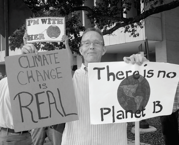 Fort Worth resident Jim Roaten holds climate change protest signs.