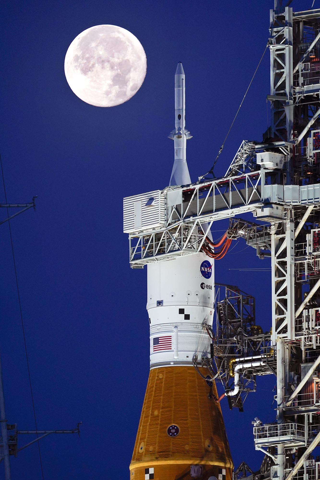 Photo of The Artemis I rocket as it sits on the launchpad at Cape Caniveral just prior to launch, with the moon in the sky above it.