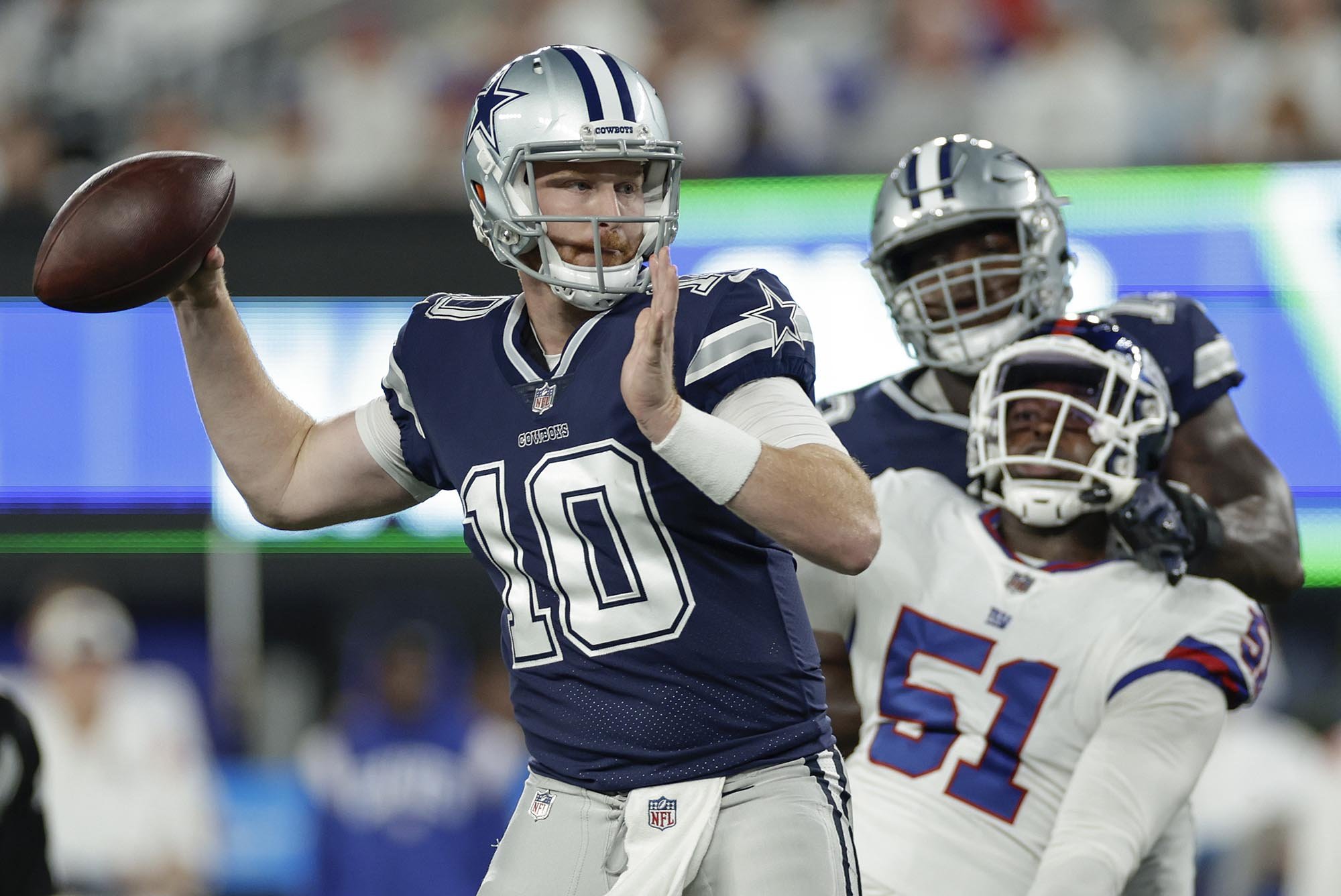 Dallas Cowboys back up quarterback Cooper Rush throws a pass while a N.Y. Giants player watches helplessly while being blocked.