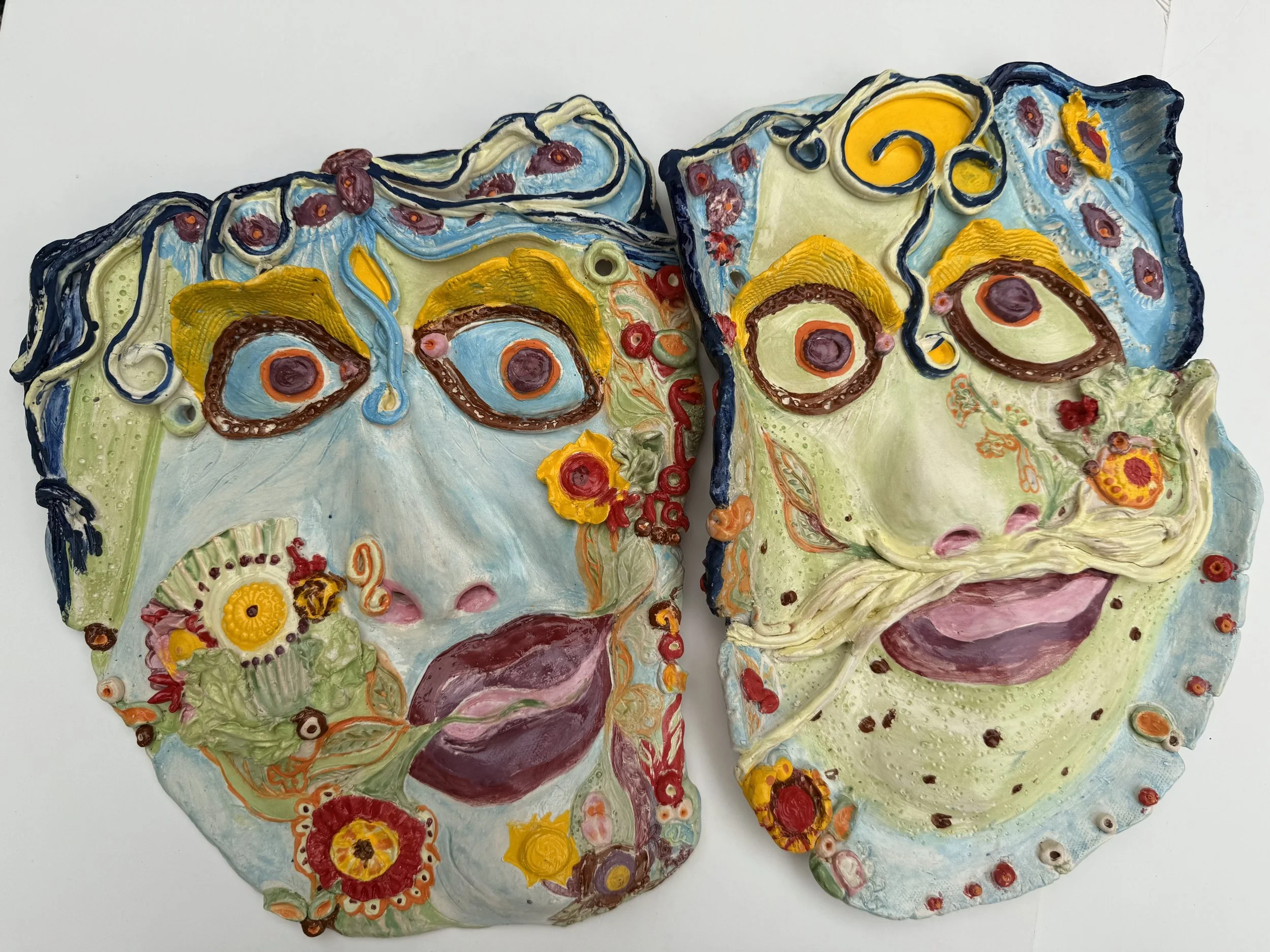 Two colorful, textured masks resembling abstract human faces with exaggerated features, vibrant colors, and intricate patterns.