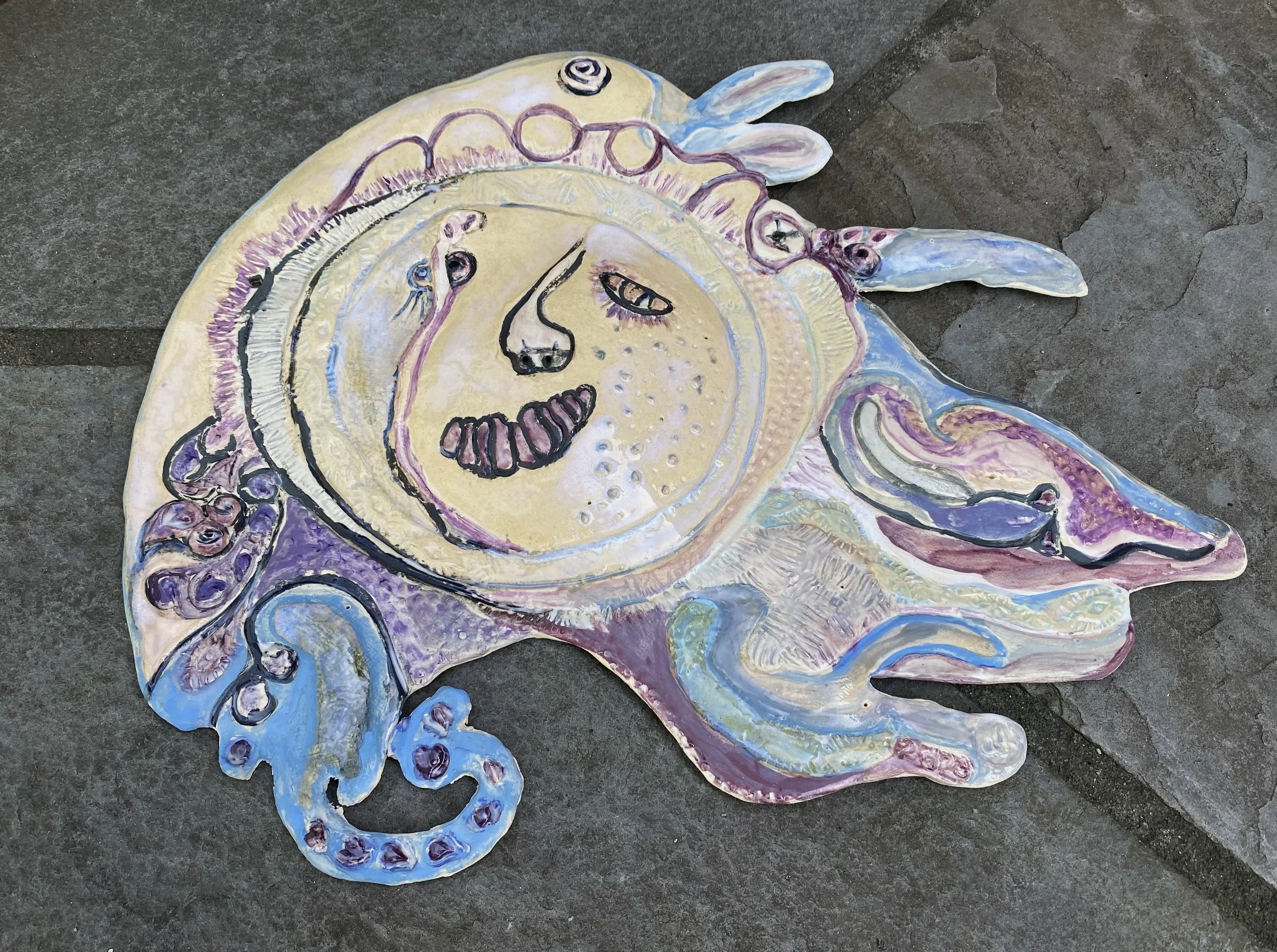 Painting of a surreal face with closed eyes, a nose, and a mouth, surrounded by abstract shapes and tentacle-like extensions in pastel colors on a rocky surface.