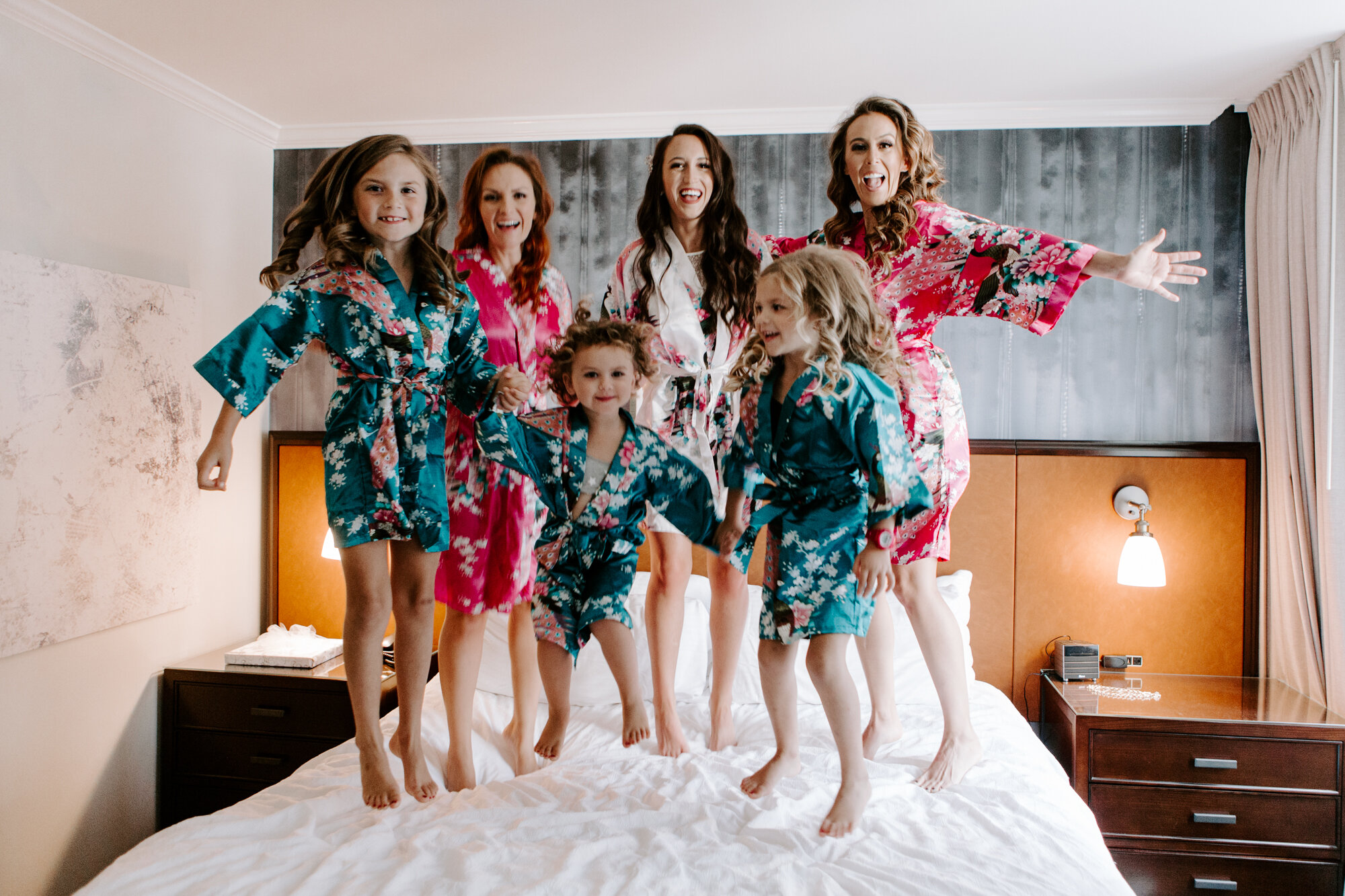 Bridal preparations. Portraits with bridesmaids and flower girls jumping in bed. Glamorous Wedding at Hotel Magnolia